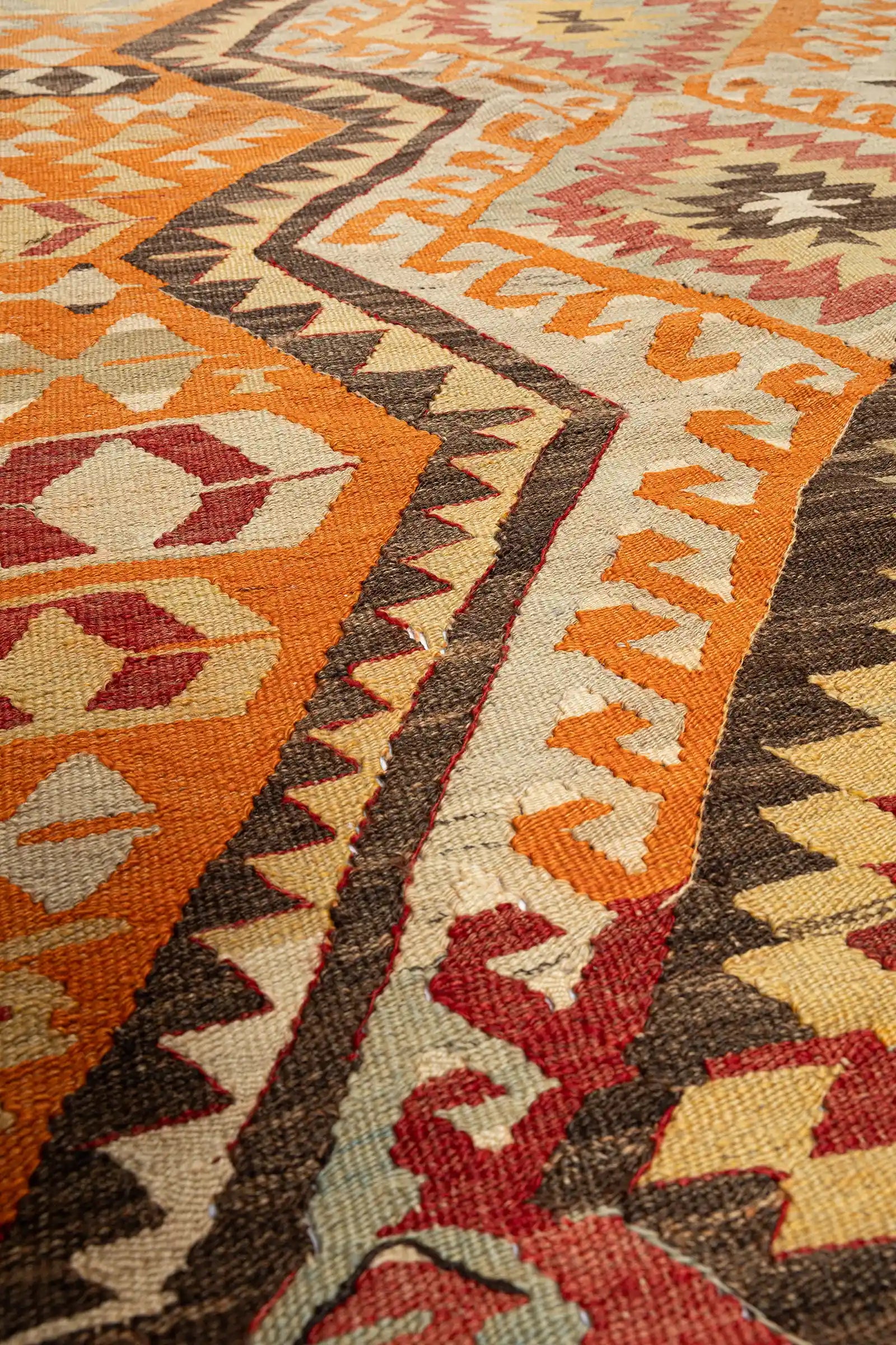 Nahaufnahme der Textur – flach gewebte Oberfläche mit dichter Wollstruktur, Farbtöne in Ocker, Beige und Terrakotta; klar abgegrenzte Musterkanten sichtbar