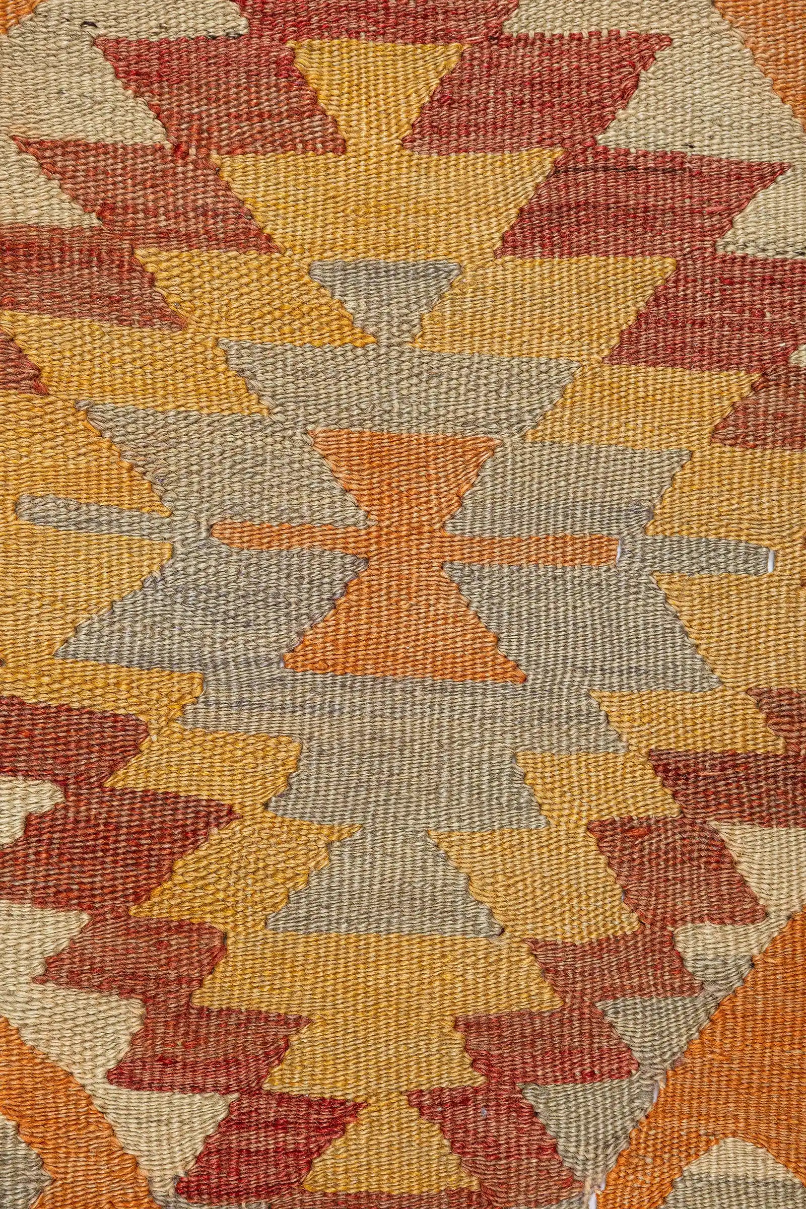 Detailaufnahme des Rautenmusters – ineinander verzahnte, gezackte Farbfelder in Gelb, Beige, Braun und Dunkelrot auf hellem Grund, Umrandung mit oranger Linienführung und Winkelmotiven