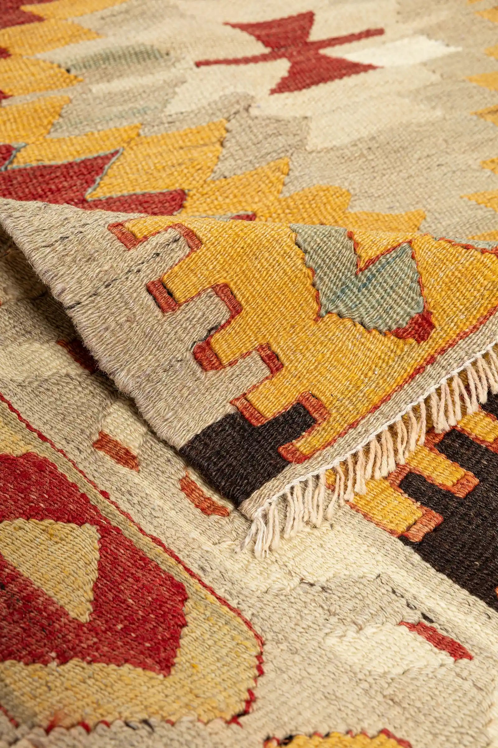 Vorder- und Rückseite im Vergleich – Ecke des Kelims umgeschlagen, Rückseite mit identischem Musterbild, Fransen aus beiger Wolle an der kurzen Seite locker gedreht