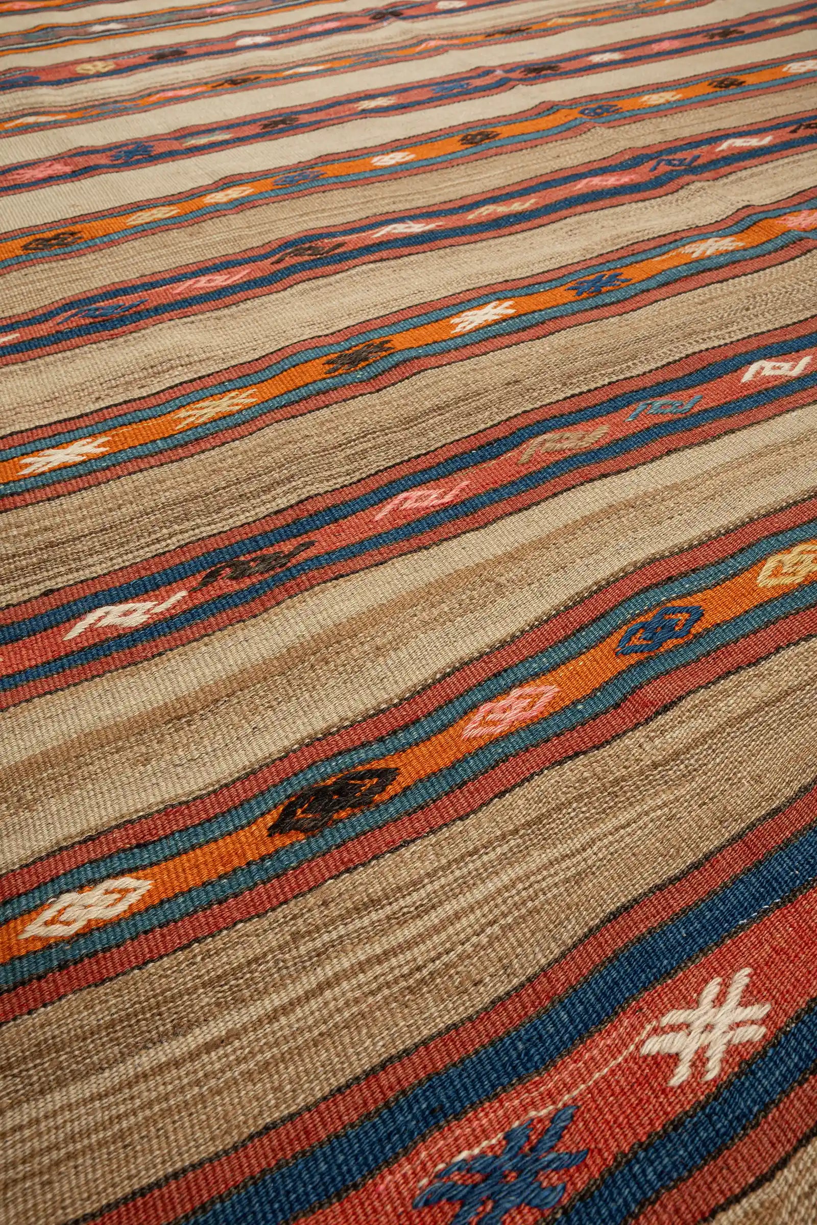 Nahaufnahme der Textur – grob gesponnene Wolle in Naturbraun mit kräftigen roten, orangen und blauen Streifen und detaillierten kleinen Ornamenten in kontrastierenden Farben