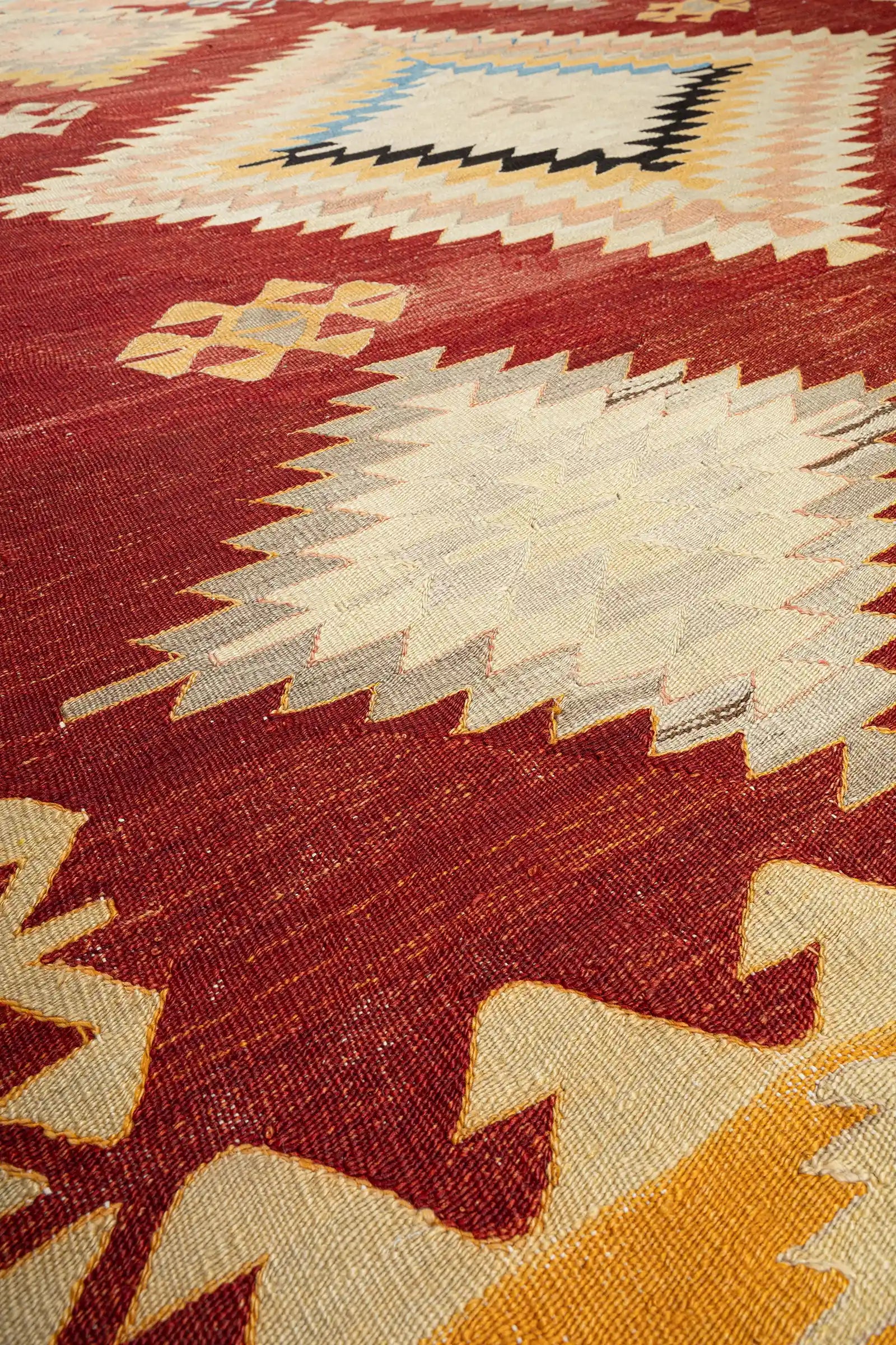 Nahaufnahme der Textur – eng gewebte Wollstruktur in hellen, naturfarbenen Tönen, feine Kontraste durch gestickte Details in Rot, Gelb und Blau