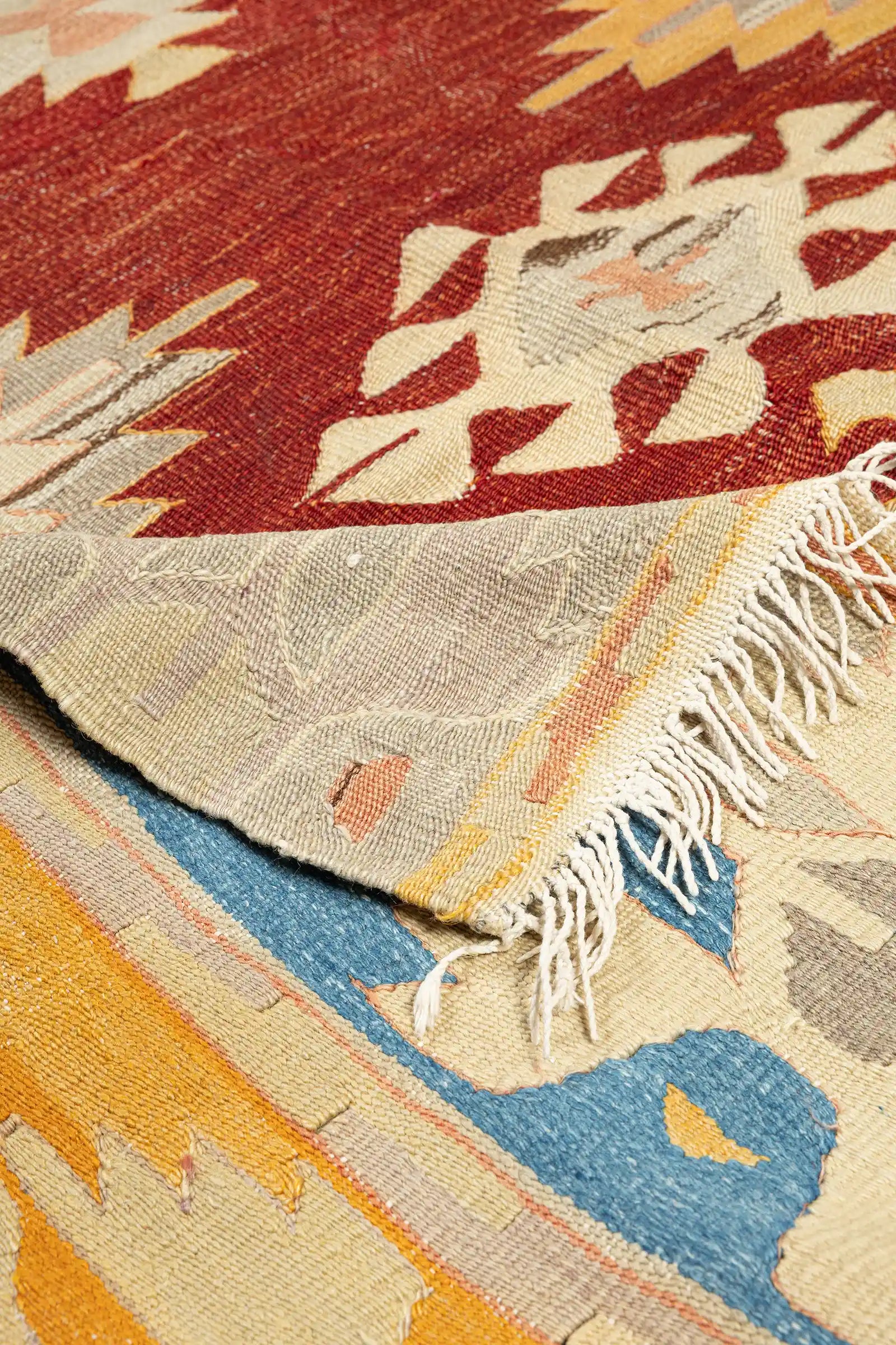 Vorder- und Rückseite im Vergleich – Ecke des Kelims leicht aufgeschlagen, Rückseite zeigt Spiegelung des Designs, Fransenabschluss in naturweiß, klare Webkante sichtbar