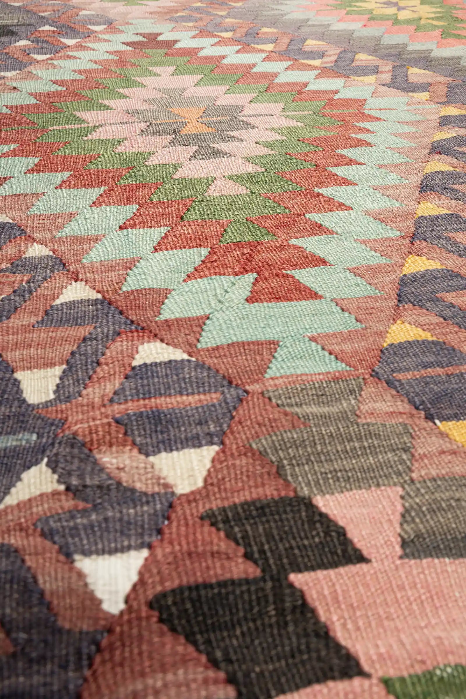 Sehr detaillierte Ansicht der Webstruktur mit Fokus auf eine zentrale Form aus dreieckigen, ineinandergreifenden Segmenten in Orange, Grau und Rosa auf dichtem Flachgewebe.