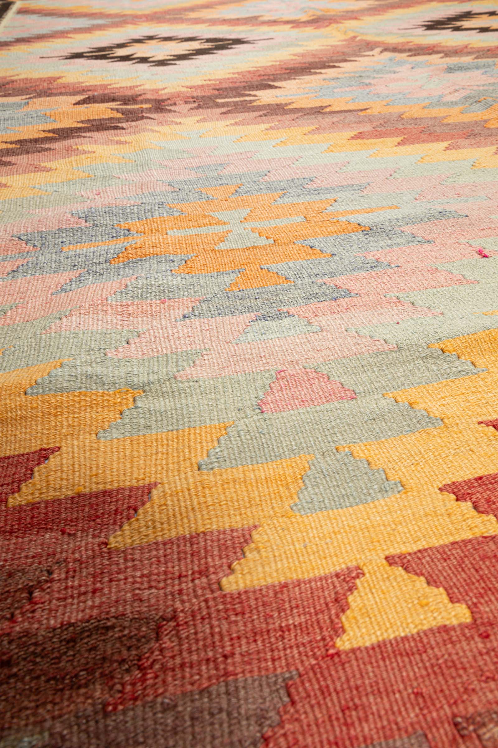 Makroaufnahme einer rosa-grauen Zickzackfläche mit beiger Kreuzform in der Mitte; feine Webtechnik und Garnstruktur gut sichtbar.