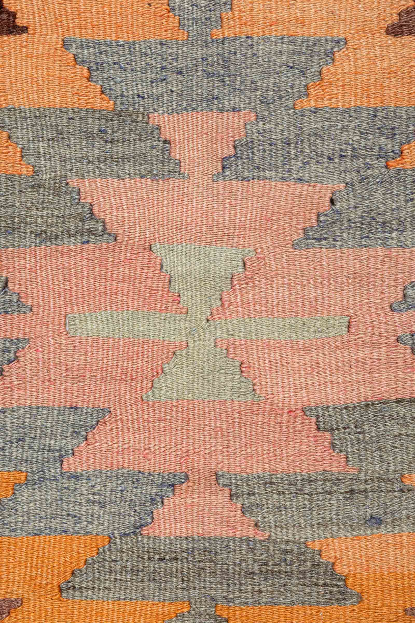 Nahansicht eines rosa-orangen Websegments mit blassen blauen und gelben Akzenten; fein erkennbare Webstruktur mit Zickzackkanten in verschiedenen Farbabstufungen.