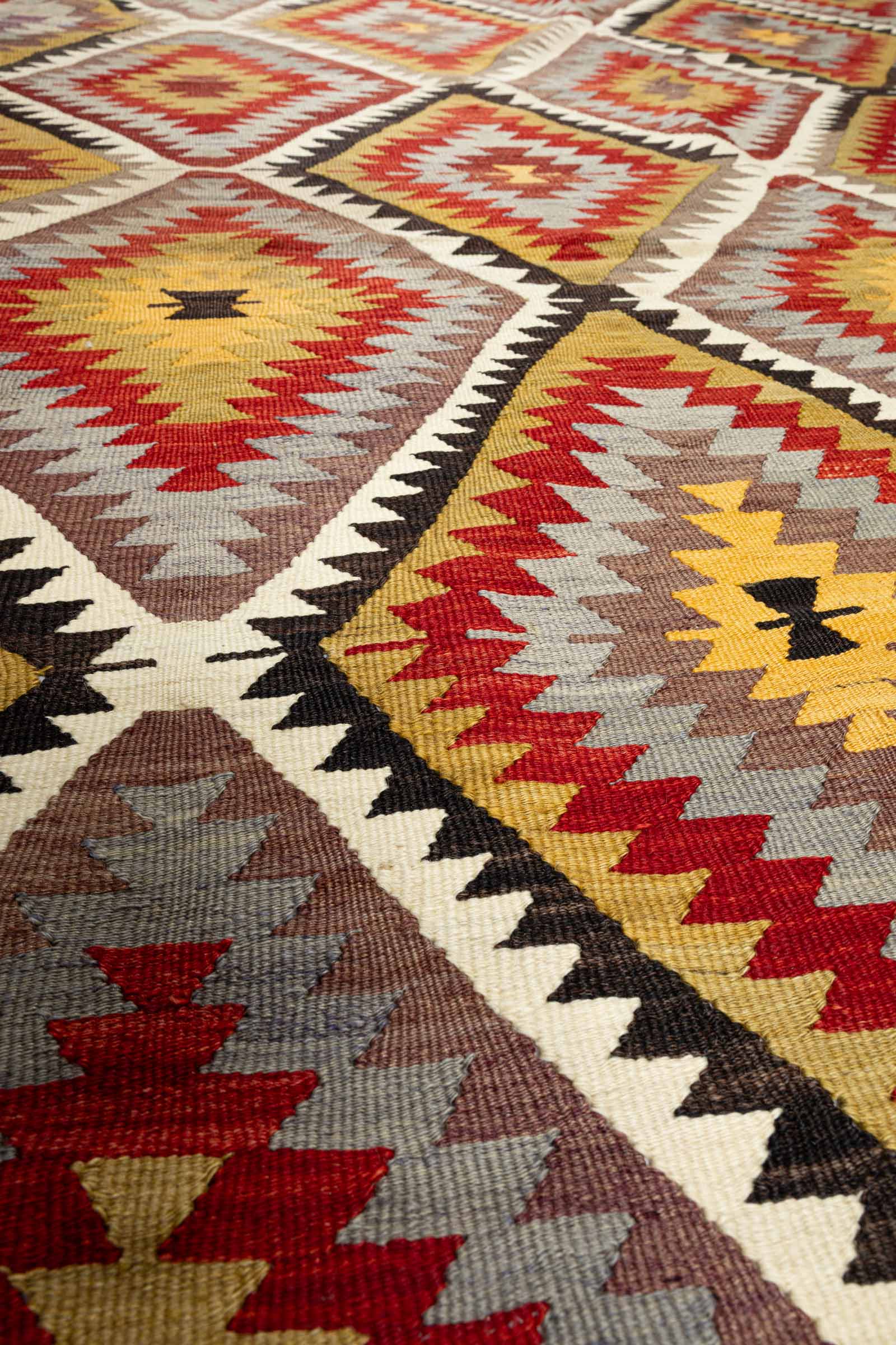 Makroaufnahme einer zentralen Rautenform mit gelbem, braunem und rotem Webgarn, deutliche Sichtbarkeit der Faserstruktur und Webtechnik.