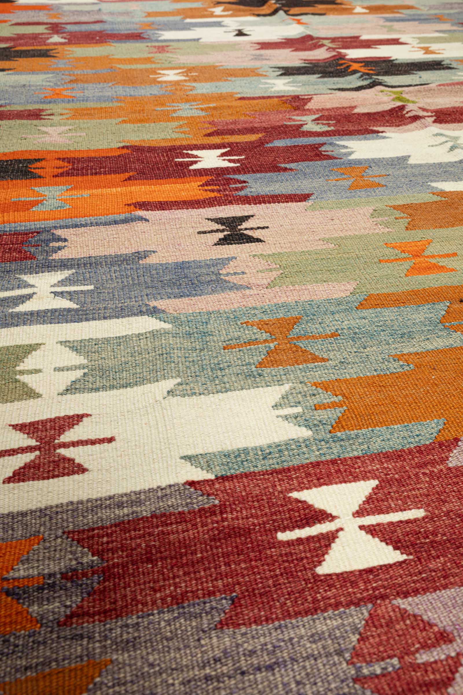 Detaillierte Ansicht der Kilim-Oberfläche mit sichtbarer Webstruktur in dichtem Flachgewebe, kräftige Farben wie Creme, Dunkelrot und Orange, scharfkantige Muster mit klarer Kantenführung.