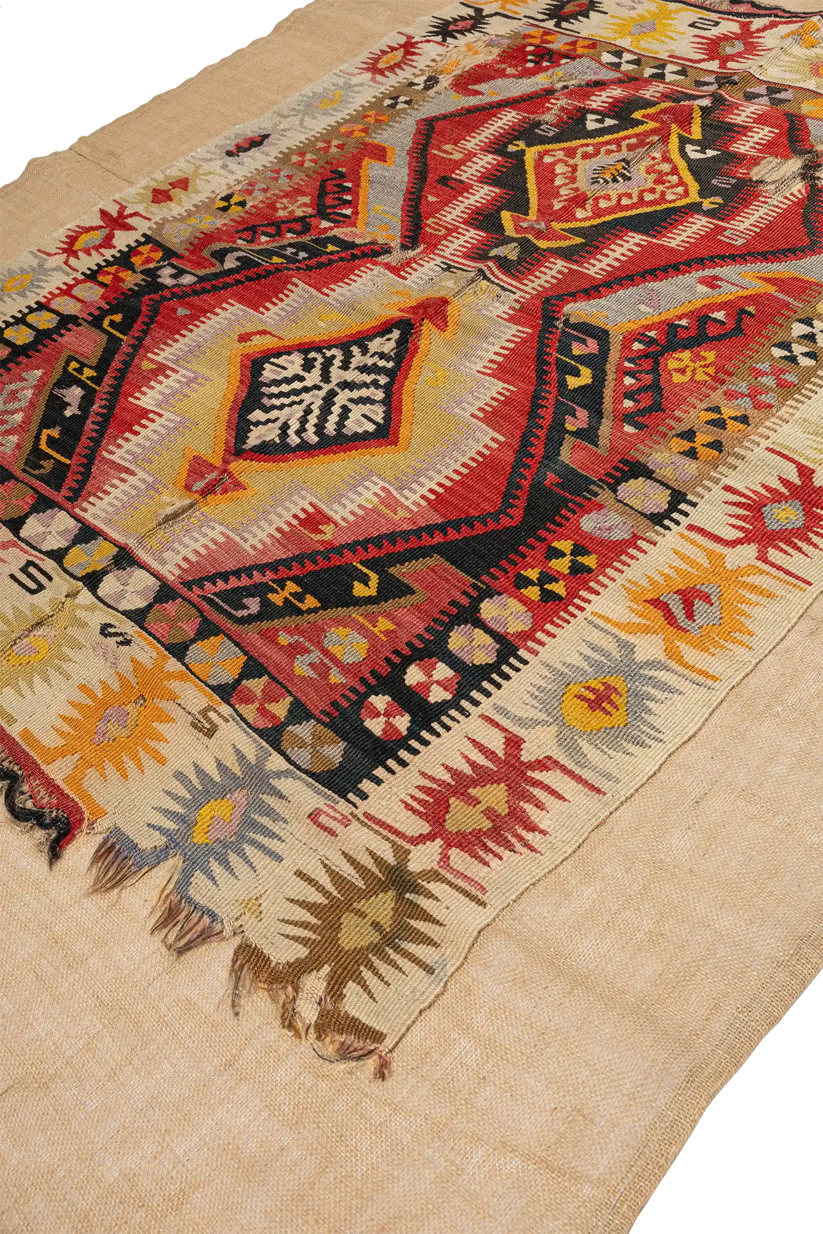 Seitlich aufgenommene Detailansicht der rechten unteren Ecke mit Blick auf die farbige Bordüre mit sternförmigen Motiven in Gelb, Braun, Blau und Rot auf hellem Grund sowie einen Abschnitt der beschädigten unteren Webkante.