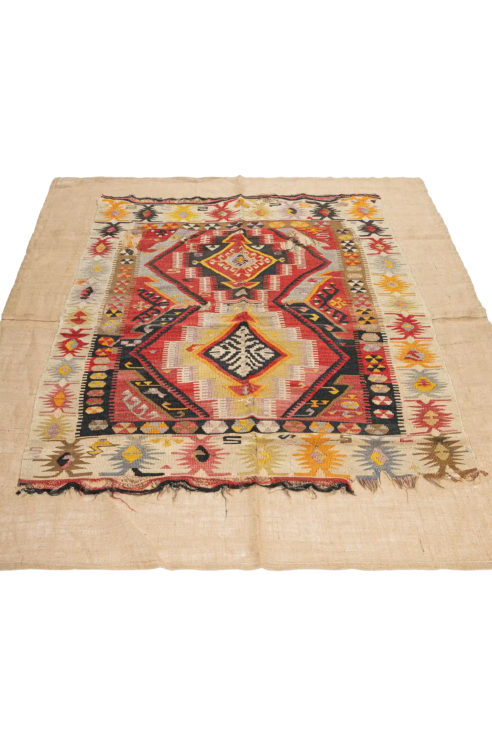 Schräg aufgenommene Ansicht des zentralen Musters, das aus komplexen Rauten und geometrischen Symbolen in lebhaften Farben wie Rot, Gelb, Schwarz und Weiß besteht. Der beigestoffige Hintergrund ist an den Seiten deutlich sichtbar.