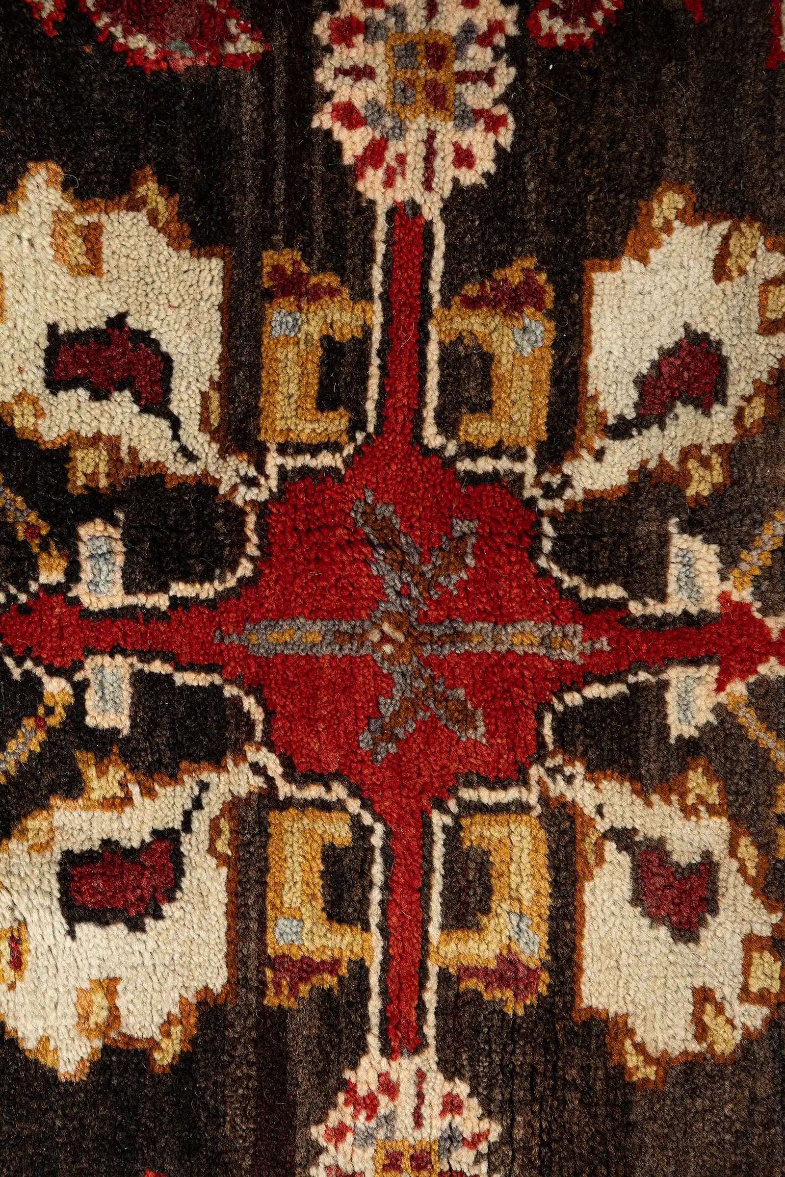 Detailaufnahme des geknüpften Medaillons – dichter Knotenaufbau mit kontrastreichen Formen in Creme, Schwarz, Ziegelrot und Ocker auf tiefem Hintergrund