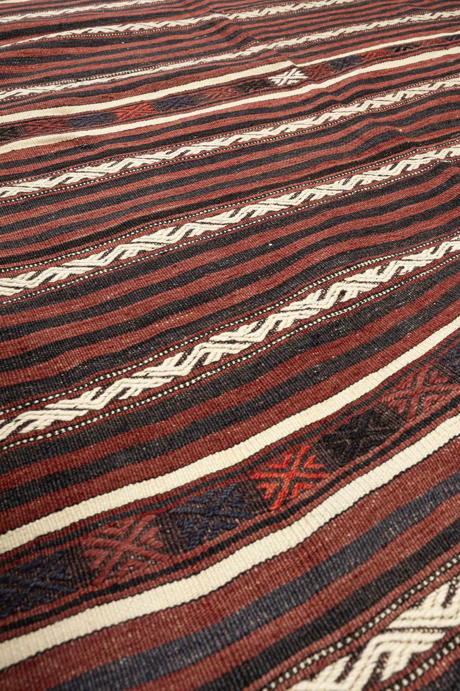 Nahaufnahme der Textur – fein gewebte Wollstruktur mit schmalen Streifen in Braun- und Schwarztönen, mittig ein plastisches weißes Band mit versetzten diagonalen Mustern