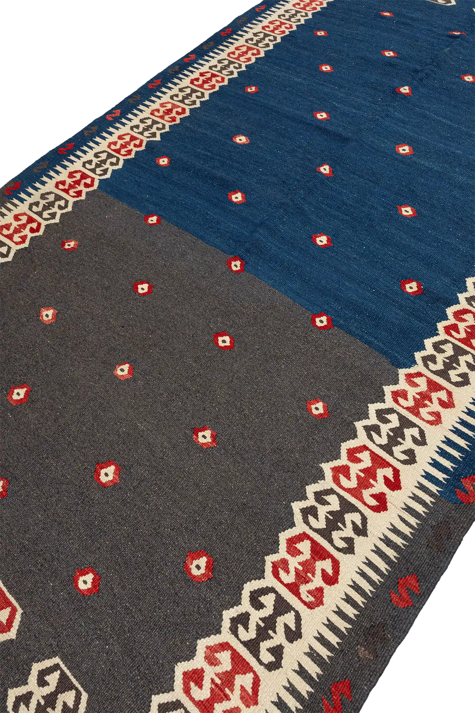 Ansicht in leichter Schräglage zeigt die textile Oberfläche und die Zweifarbigkeit des Kelims – linke Hälfte in dunklem Grau, rechte Hälfte in tiefem Blau mit gleichmäßig verteilten roten Blütenmotiven.