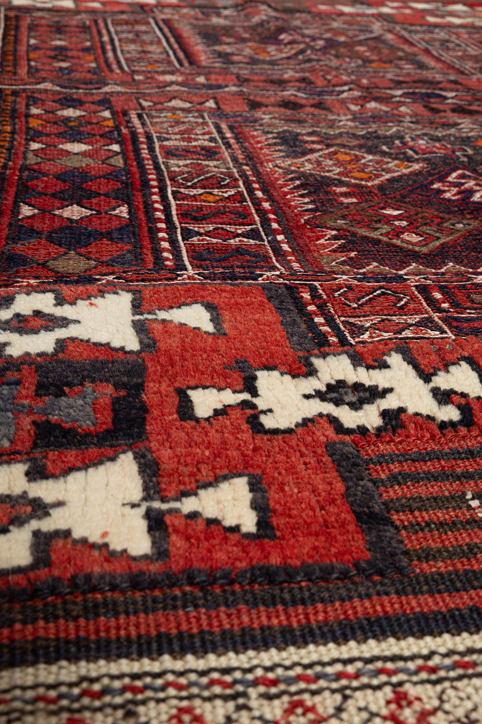Detailausschnitt eines zentralen Rautenmusters auf dunkelrotem Grund. Die dichte, leicht flauschige Textur des Kilims ist klar erkennbar; eingewebte symmetrische Ornamente in Weiß, Dunkelrot, Ocker und Schwarz kontrastieren scharf.