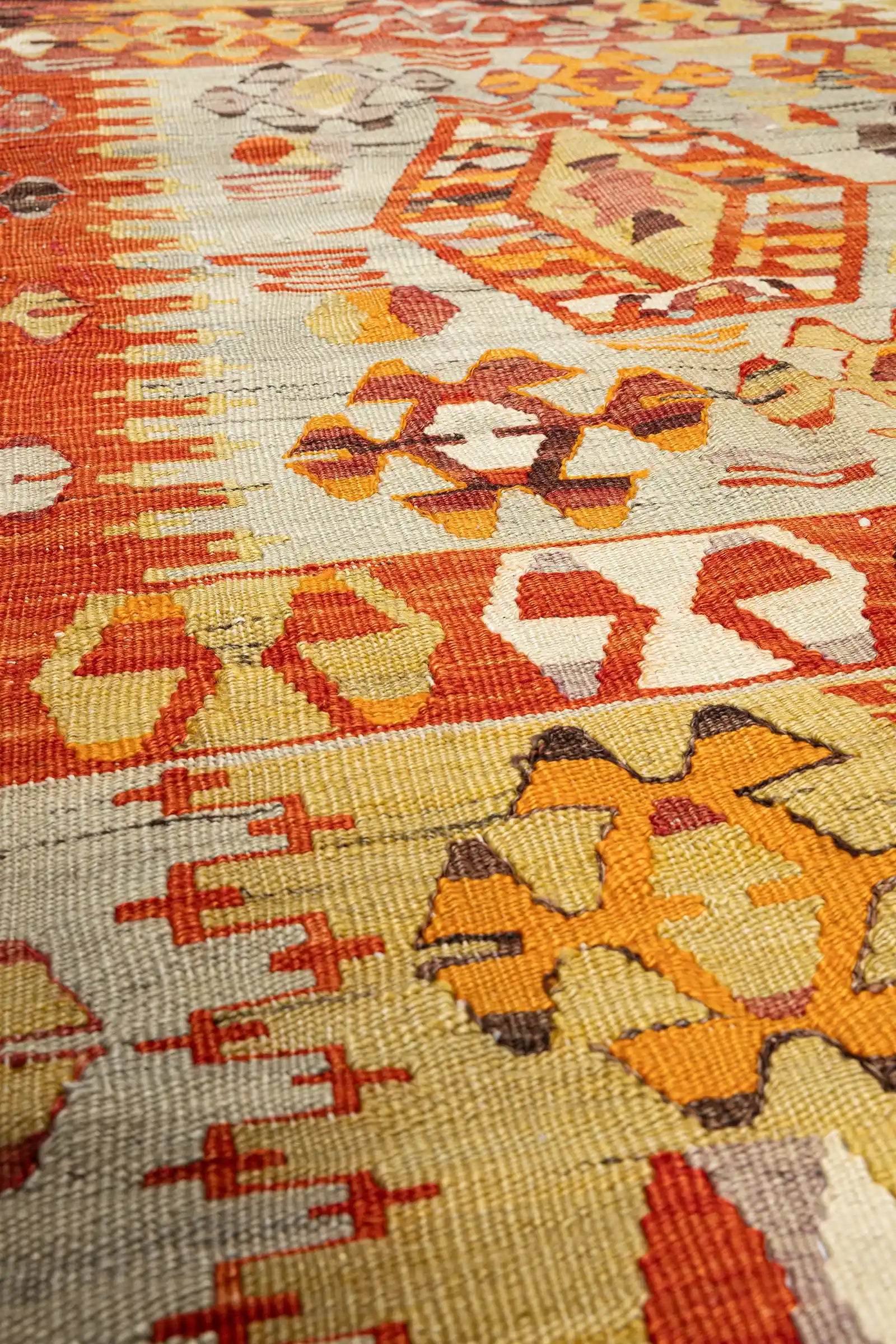 Detaillierter Ausschnitt des zentralen Medaillons mit eng gewobener Flachgewebestruktur; gut sichtbare Wollfaserverläufe in Rot, Olivgrün, Ocker und Violett.