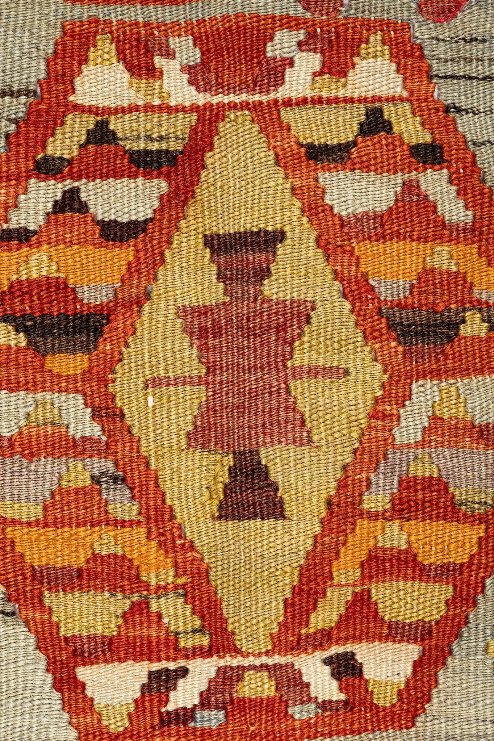 Nahansicht eines Sechseckmotivs mit gezacktem, rot-gelben Innenfeld auf hellolivgrünem Hintergrund, eingerahmt von rot-orangenen Treppenmustern und flankiert von farbenfrohen Symbolformen.