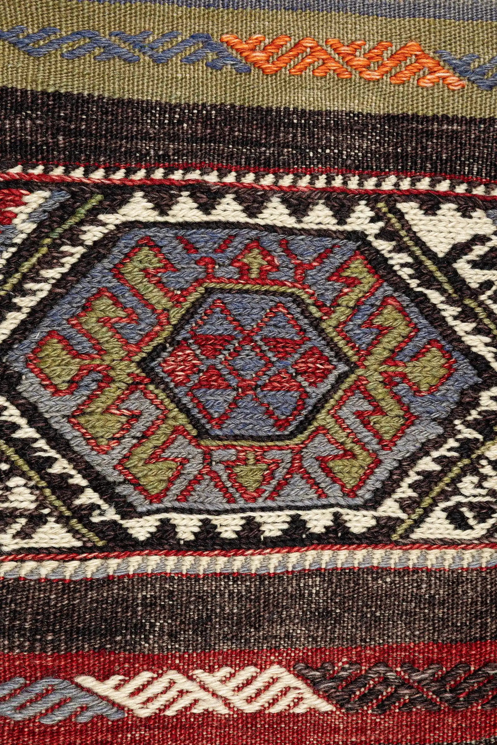 Detailaufnahme eines hexagonalen Zentralelements – geometrisch gerahmtes Feld mit mehrfarbigen Webdetails in kühlem Blau, Rot, Oliv und Schwarz auf elfenbeinfarbener Kontur