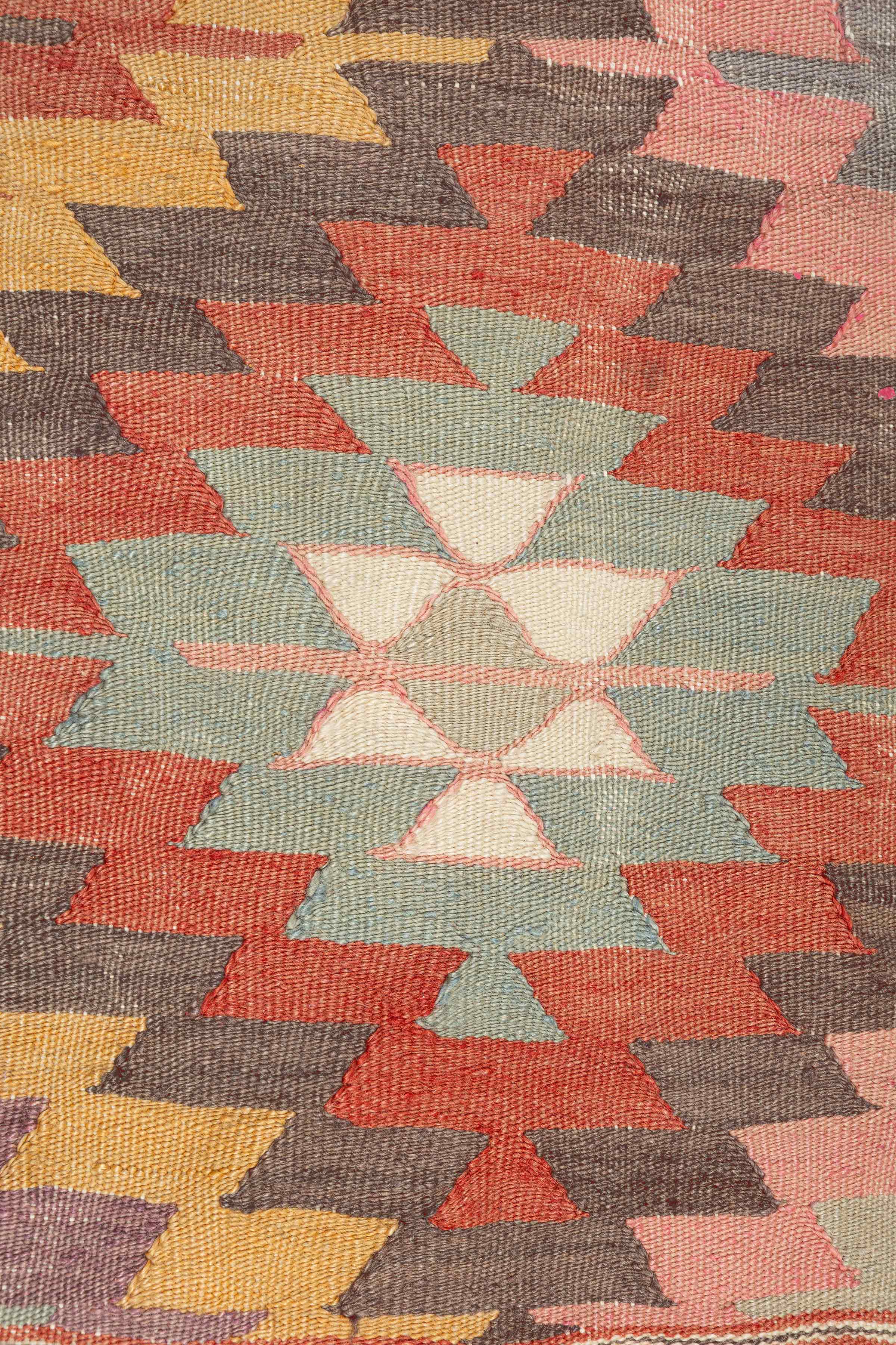 Nahaufnahme der handgestickten Cicim-Symbole in Lavendelrosa, Safrangelb und Ziegelbraun auf naturfarbener Wolle