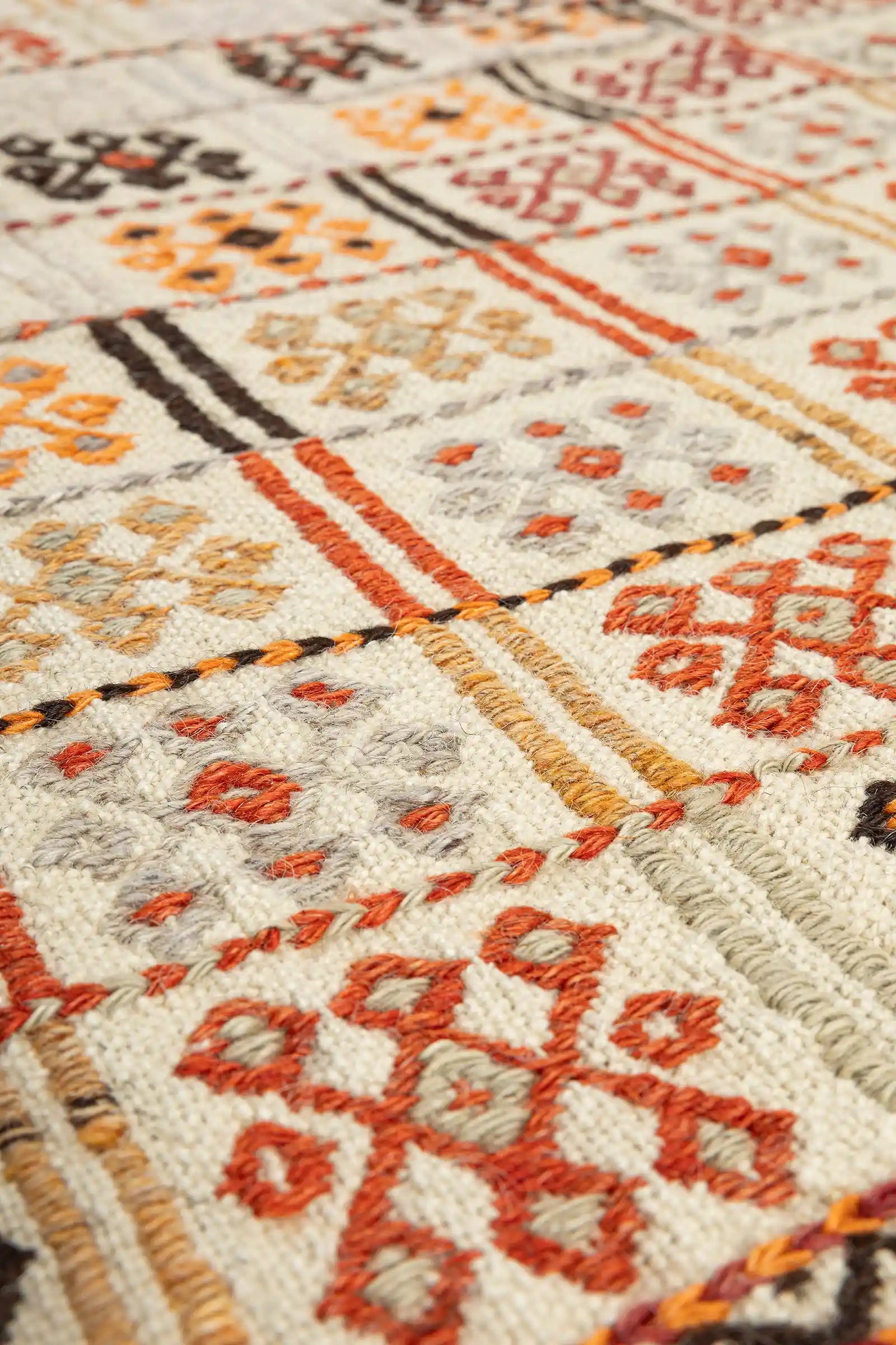 Detailaufnahme eines kleinen Rechtecks mit orangefarbenem Symbol auf heller Grundfläche; sichtbare Wollstruktur mit dichter, leicht erhobener Stickerei in klar abgegrenzter Farbgebung.