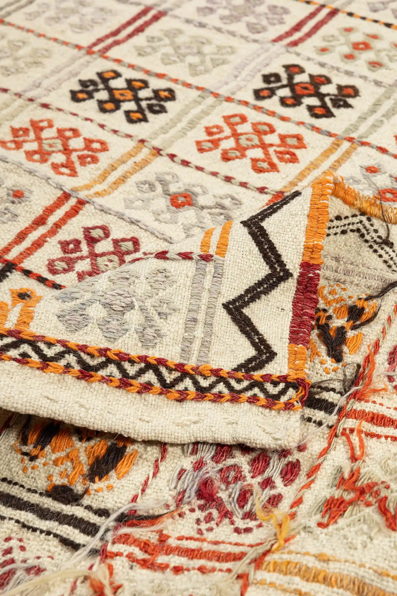 Ecke des Kilims nach oben geschlagen: oben die klar abgegrenzte Vorderseite mit strukturiertem Motiv; unten die Rückseite mit lockereren Fäden, bunten Garnverläufen und dichter, naturweißer Webkante mit kurzen Fransen.