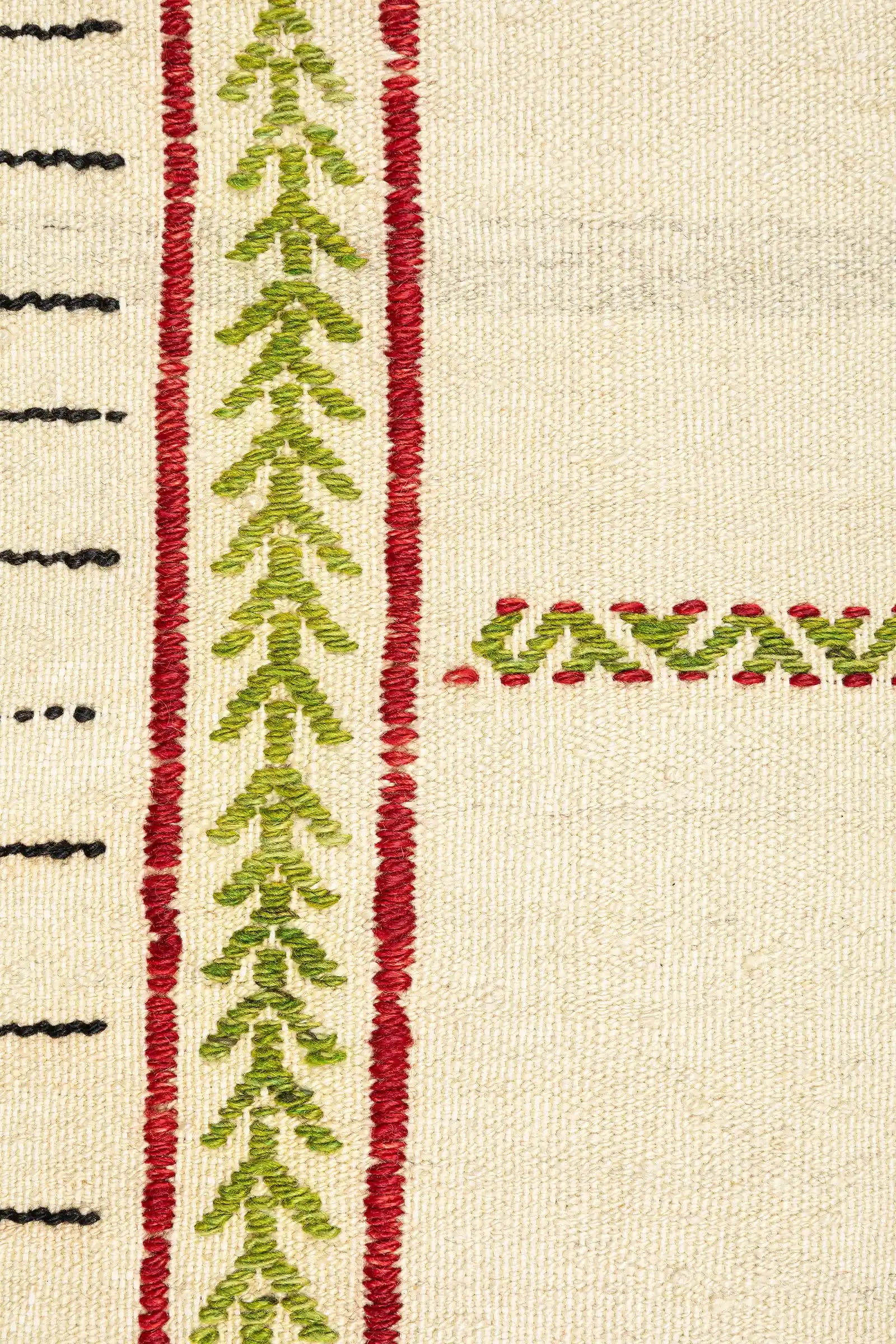 Detailaufnahme der Bordüre – feine Stickstruktur in Grün und Rot entlang der Seitenkanten, eingebettet auf hellem Gewebe