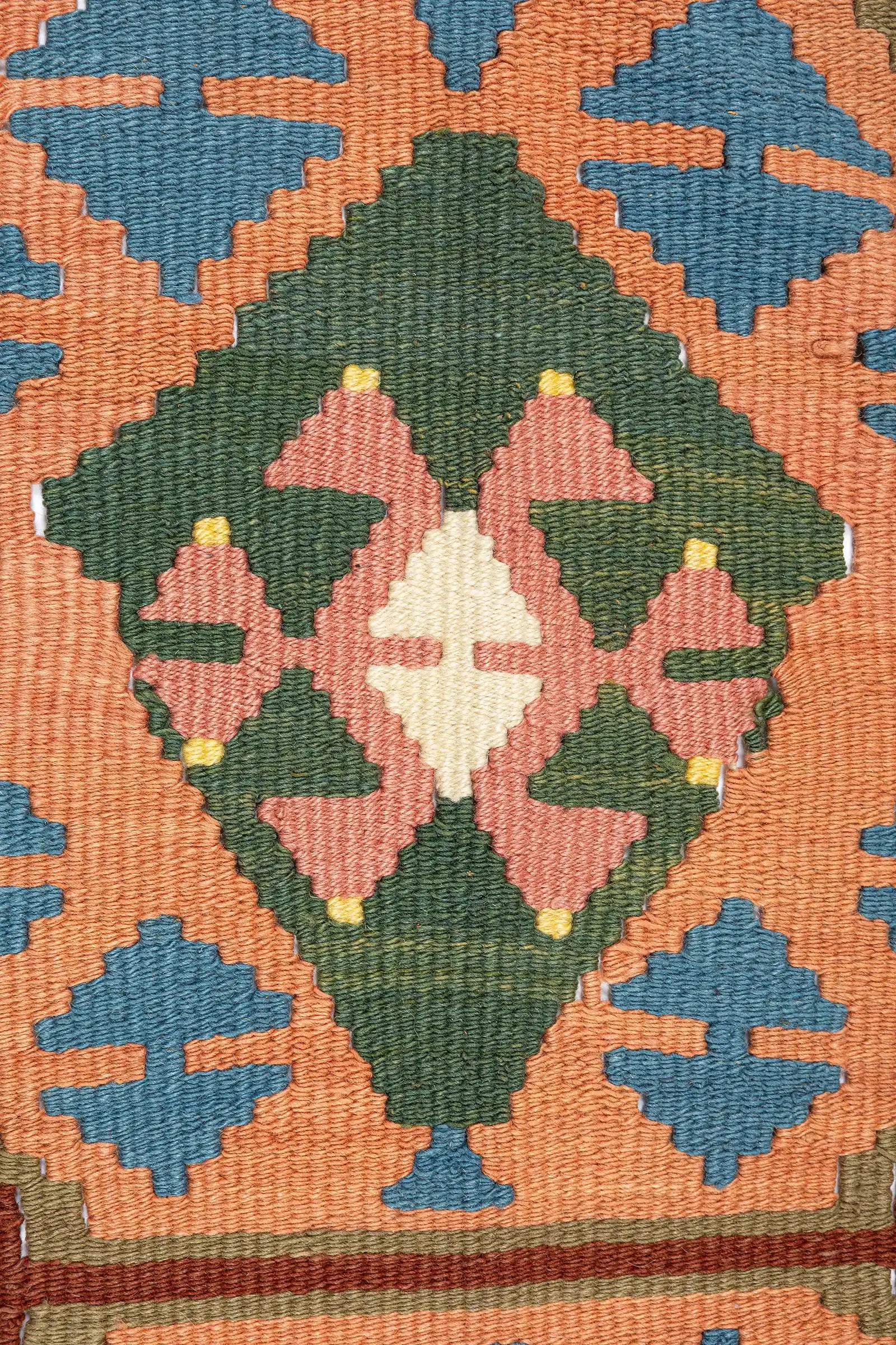 Detailaufnahme des zentralen Rautenmotivs – gewebte florale Formen in Rosé und Creme, eingefasst in ein sattgrünes Rhombusfeld mit betonten Eckmotiven in Orange und Blau