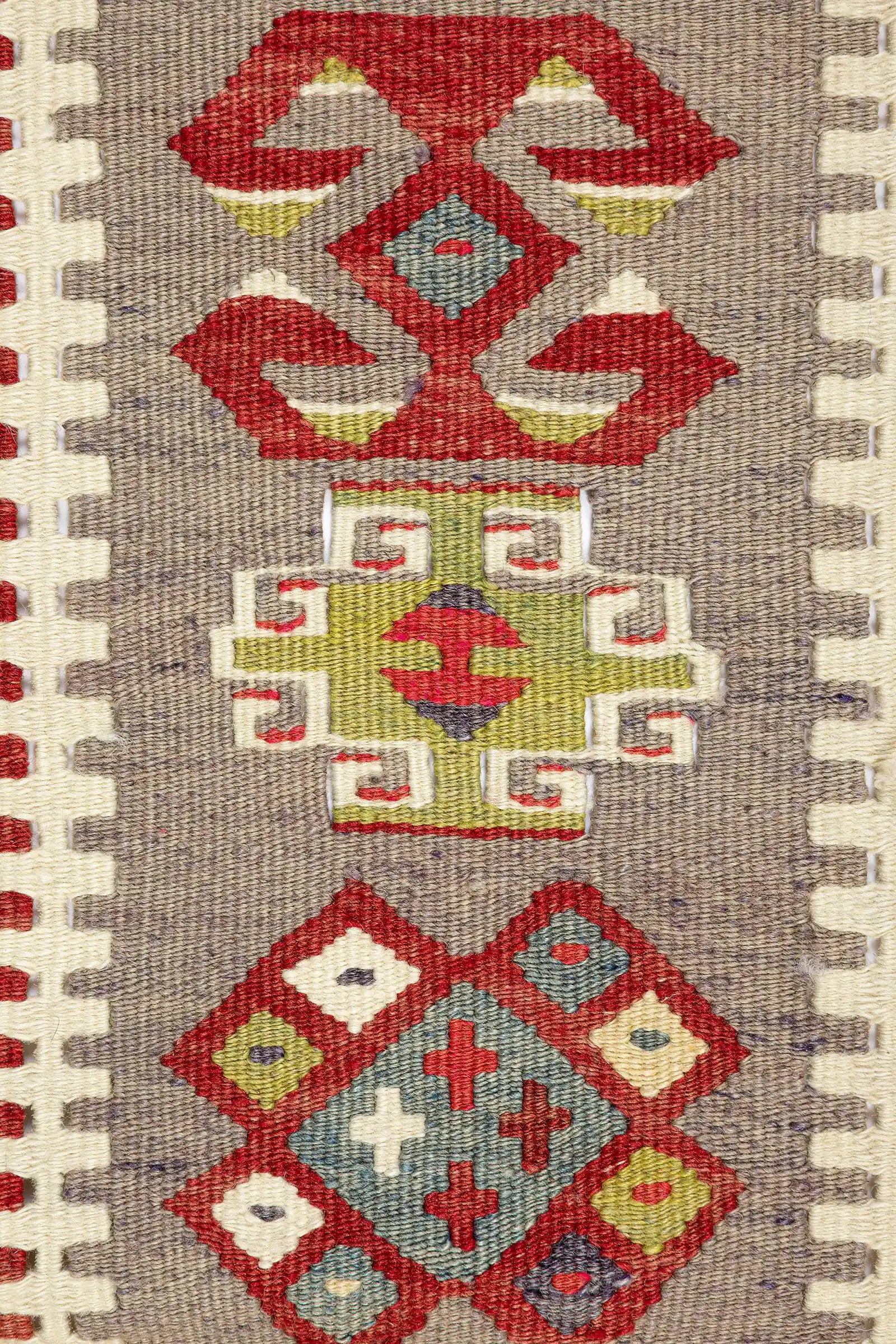 Detailaufnahme der seitlichen Bordüre – drei geometrische Motive auf grauem Grund: oben ein rotes, symmetrisches Muster mit grünem Zentrum; mittig ein olivgrünes Quadrat mit eingerückten Ecken und rotem Rhombus in der Mitte, eingefasst von cremefarbenen Winkelelementen; unten ein rautenförmiges Motiv mit rotem Rahmen und kleineren Rauten in Weiß, Gelb, Blau und Rot auf hellblauer Fläche