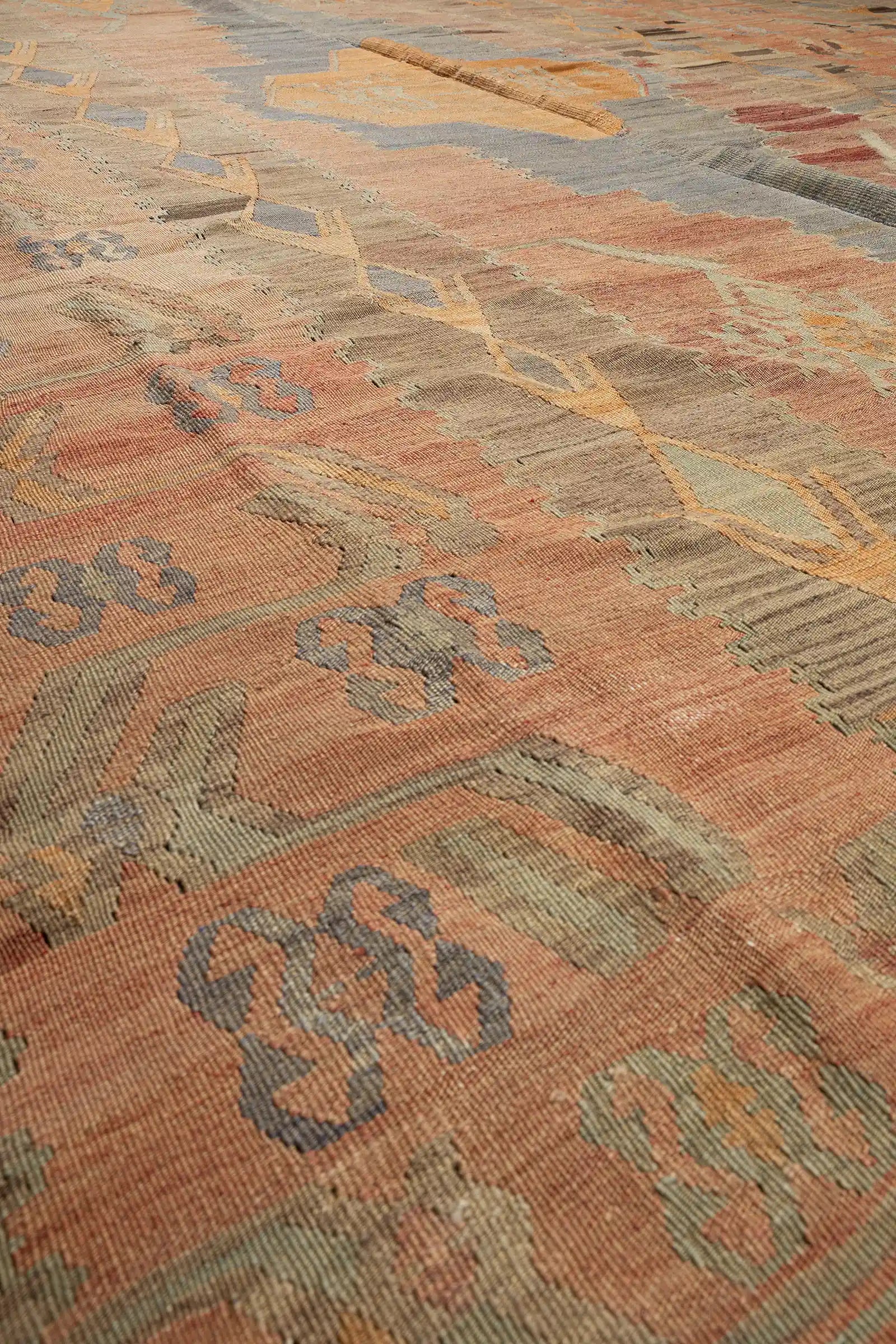 Stark vergrößerte Ansicht eines orangefarbenen Rautenmotivs mit fein sichtbarer Webstruktur aus flach gewebten Wollfäden in Blaugrau, Beige und Rostbraun.