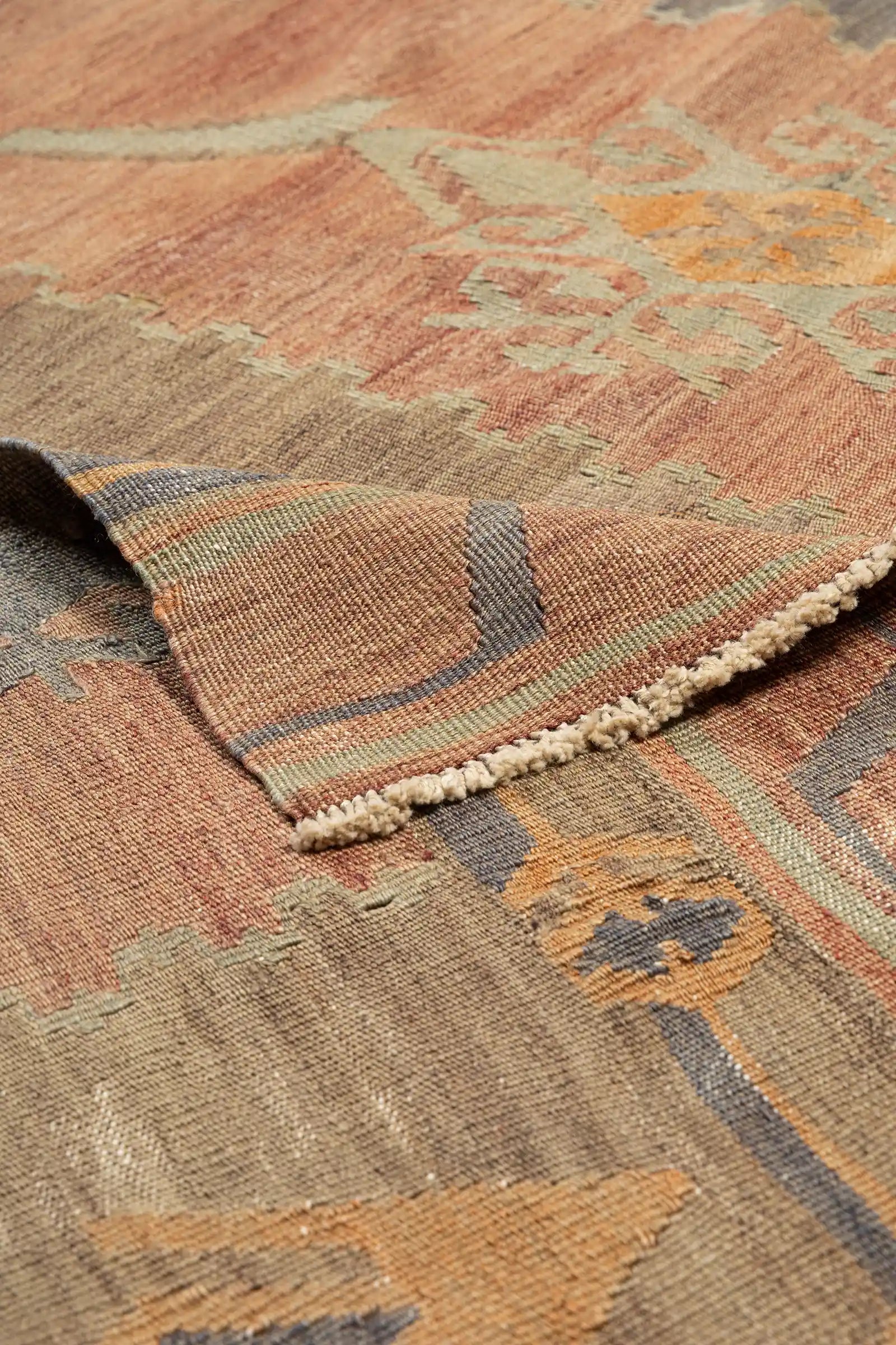 Detailansicht einer umgeschlagenen Ecke mit Sicht auf die Rückseite des Teppichs in gestreifter Webung, inklusive kurzer, naturweißer Fransen entlang der Webkante.