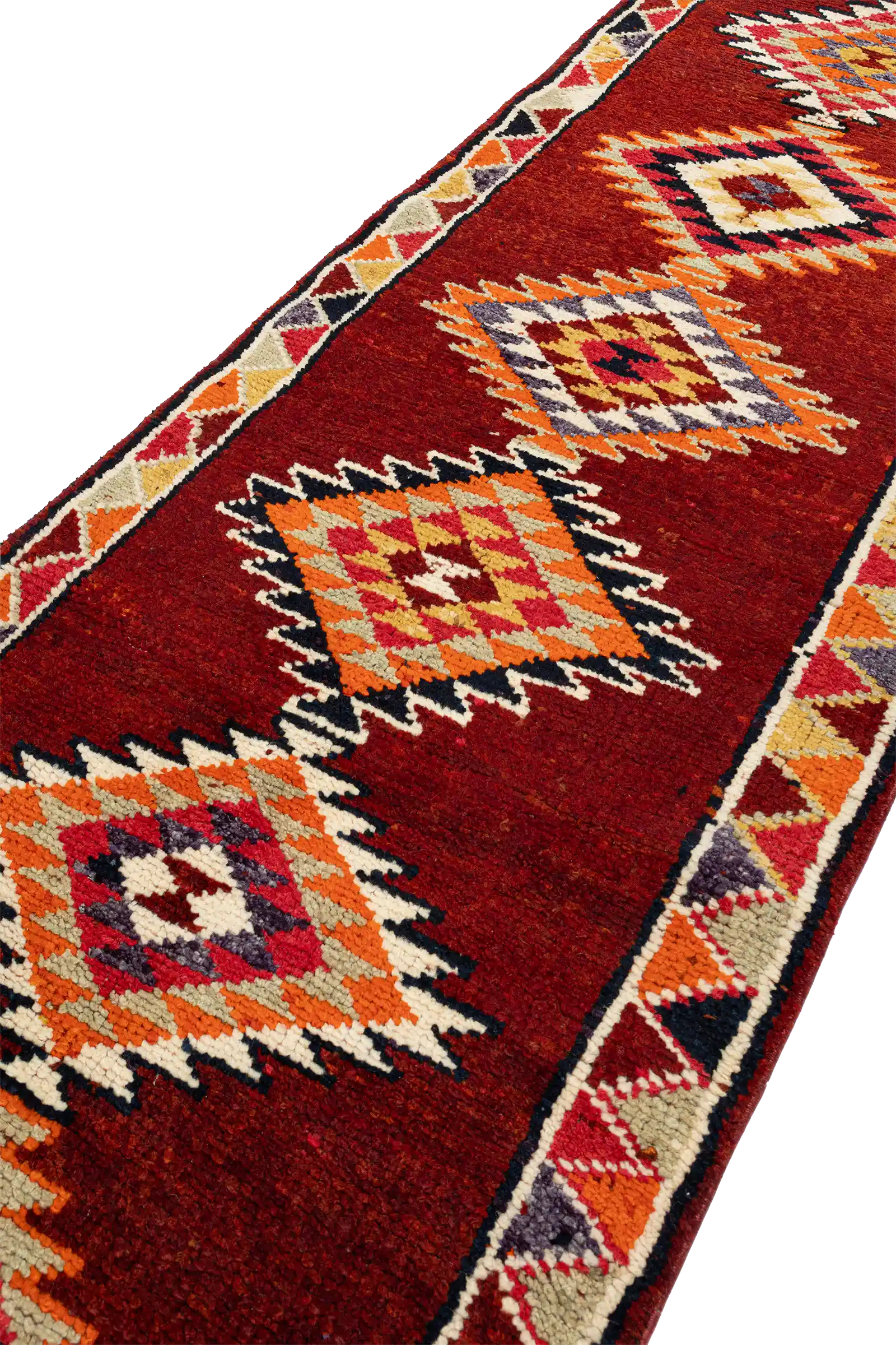 Seitliche Aufnahme eines rautenförmigen Musters mit gezacktem, mehrfarbigem Rand auf rotem Untergrund, mit sichtbaren Details der Webstruktur und Umrandung.