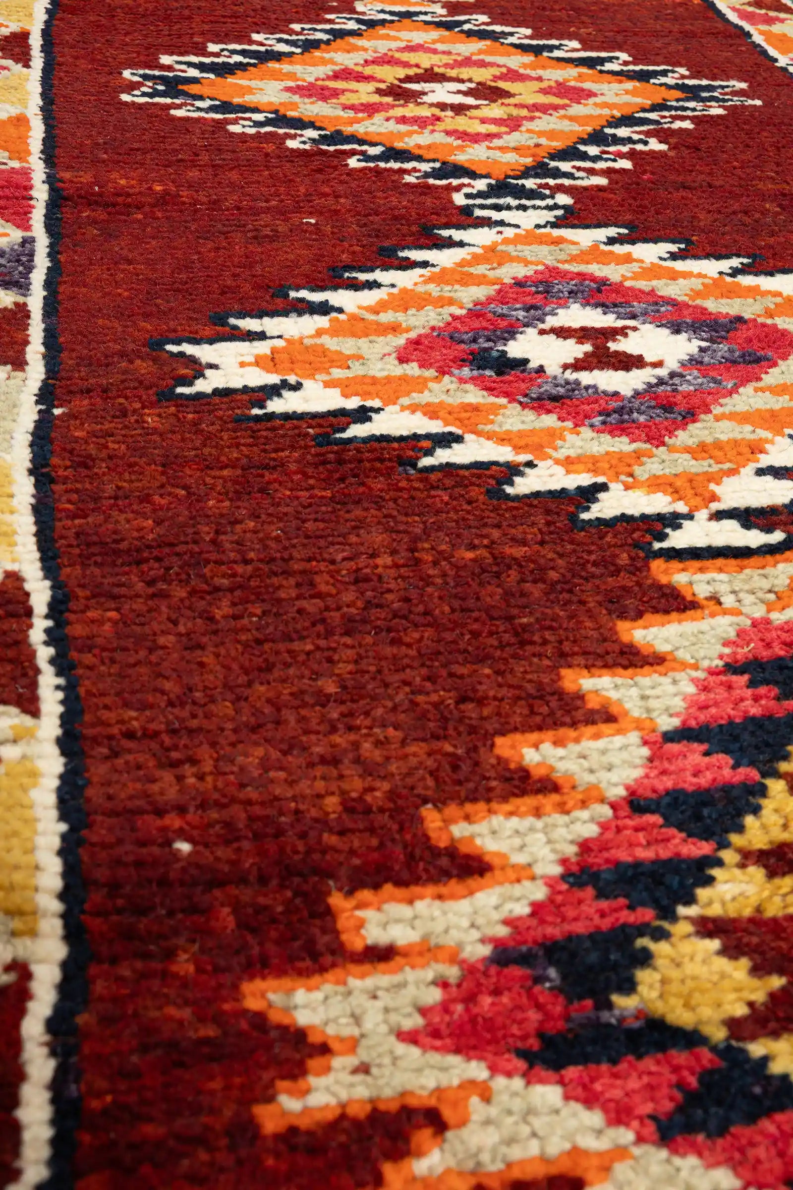 Extrem naher Ausschnitt eines Rautenmotivs mit dichter Wollstruktur und kontrastierenden Farbbereichen in Creme, Dunkelrot, Lila und Schwarz.