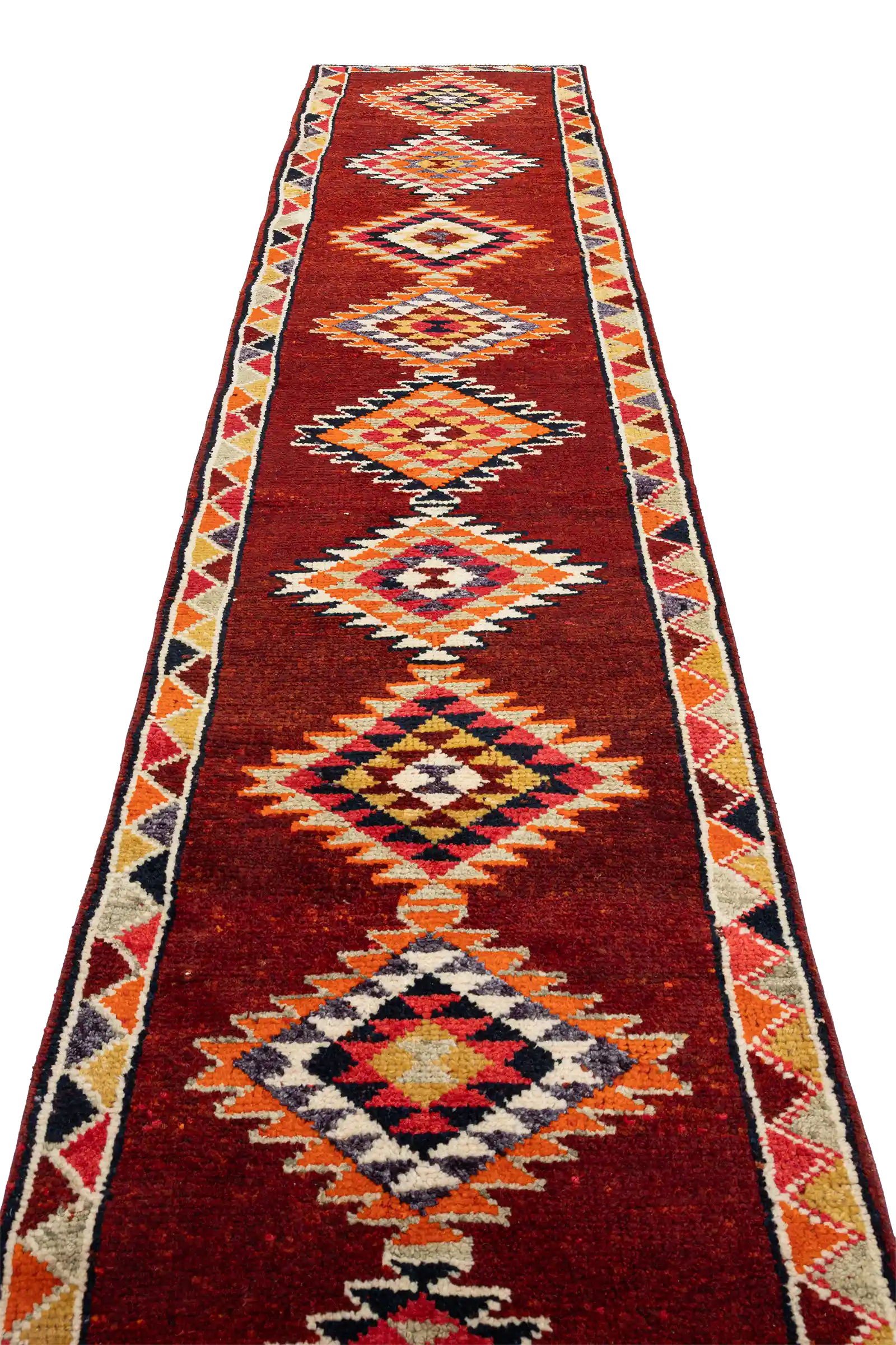 Schräger Blick entlang der Längsachse des Teppichs mit auffällig farbigen, rautenförmigen Zentralmotiven auf einem tiefroten Grund und beidseitigem Randmuster in geometrischer Ausführung.