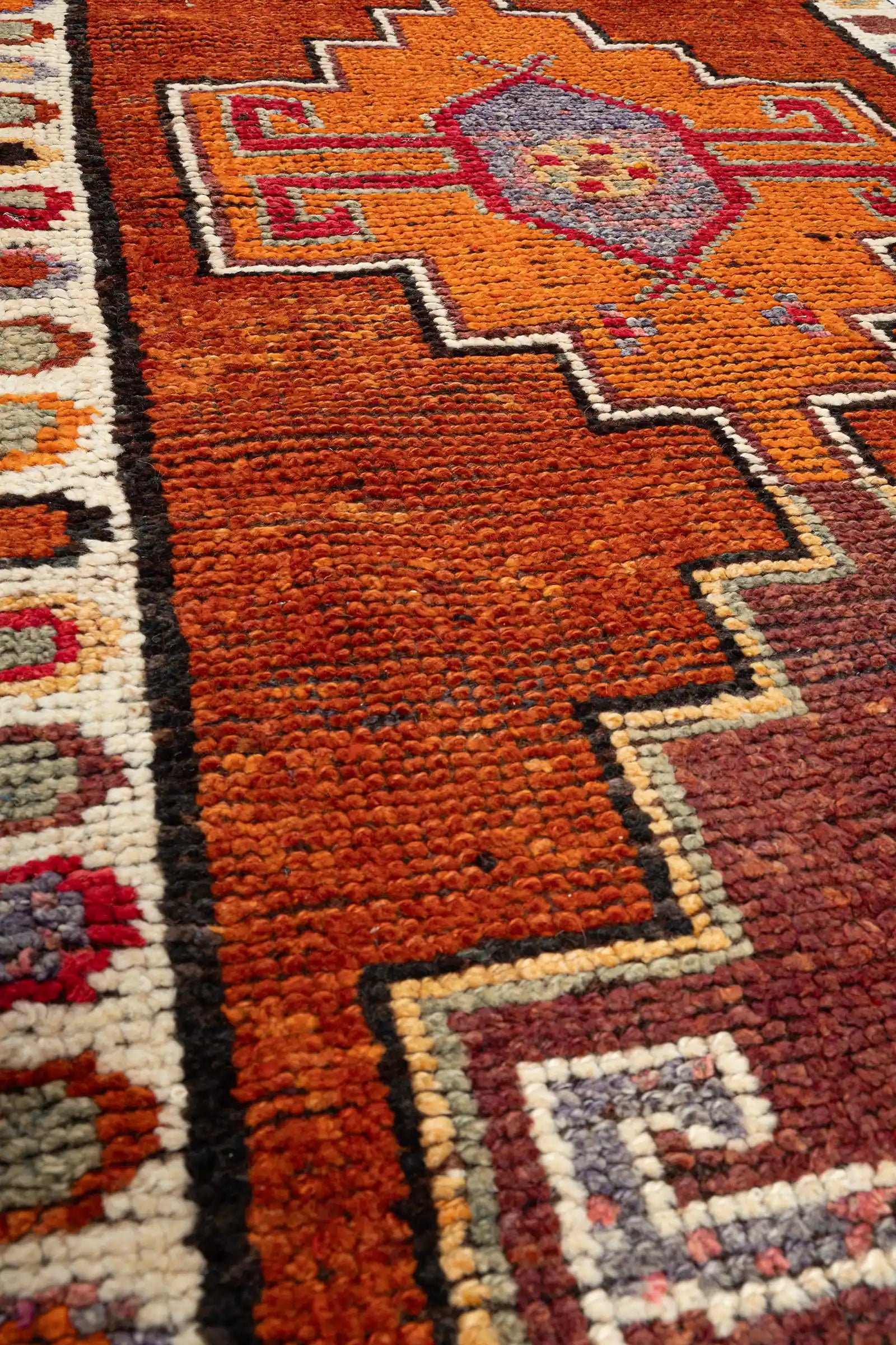 Sehr naher Blick auf ein kleines Medaillonelement mit dichter Wollstruktur in Violett, Gelb, Rot und Rosa, zeigt die feine Knüpfung und die leuchtende Farbkombination.