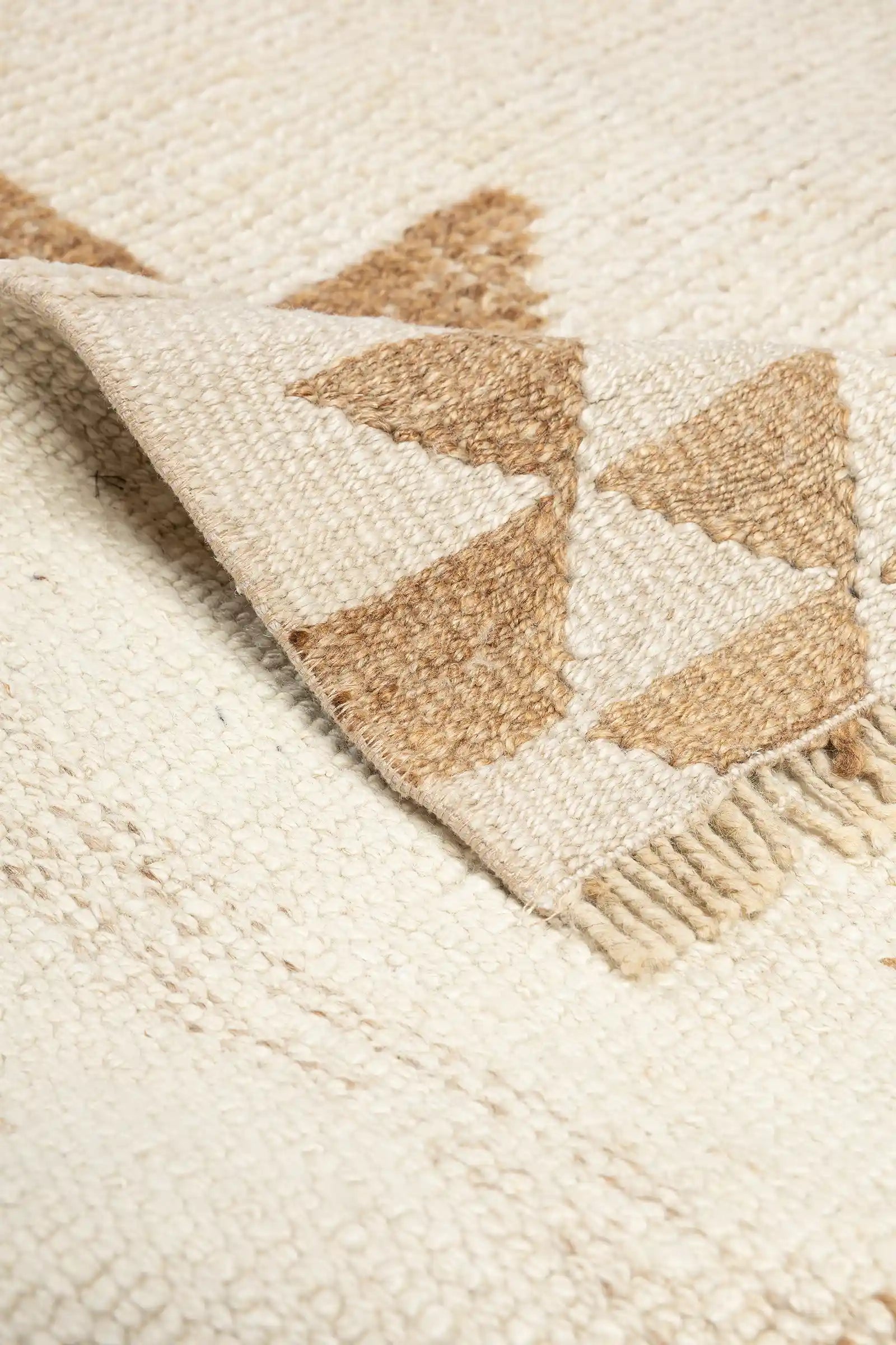 Detailbild einer umgeschlagenen Ecke des Teppichs mit Sicht auf die Rückseite in gestreifter Webung und kurzen, fein geknoteten Fransen.
