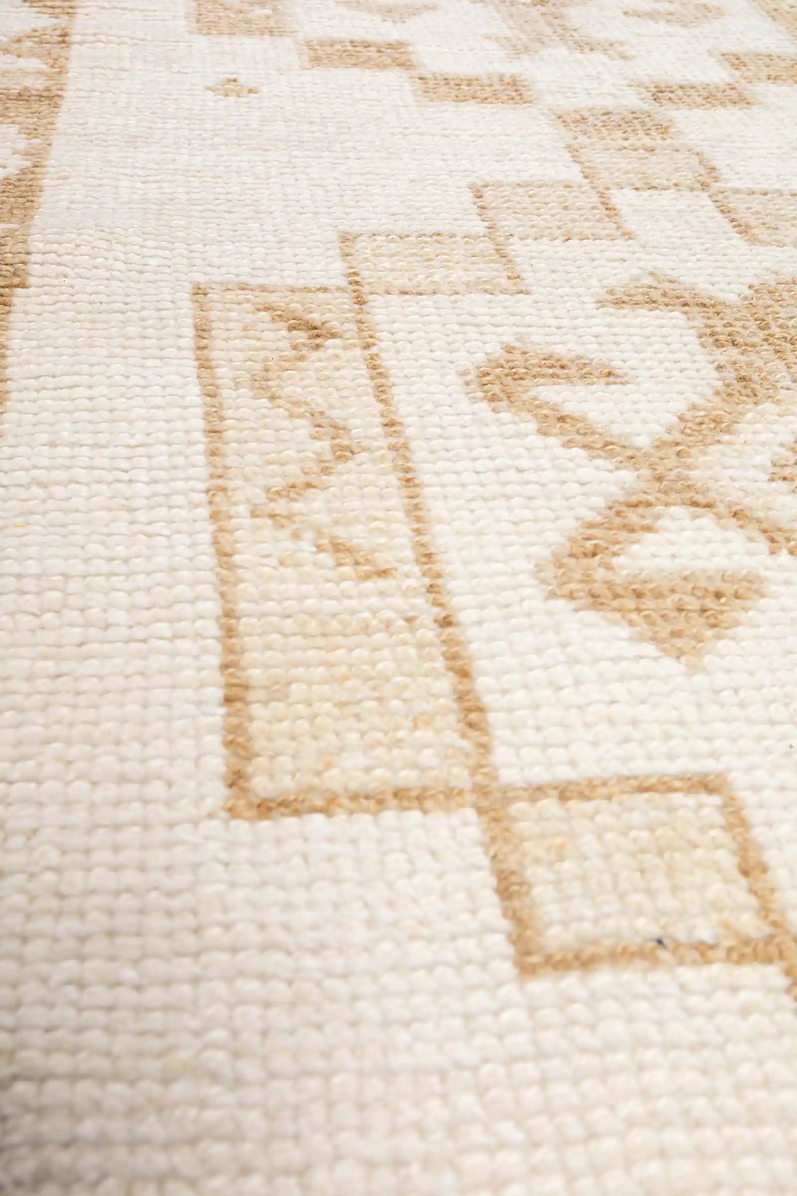 Schräger Blick entlang der Mittelachse des Teppichs mit mehreren rechteckig gerahmten Zentralmotiven, die in beigen Farbverläufen in den hellen Fond eingewebt sind.