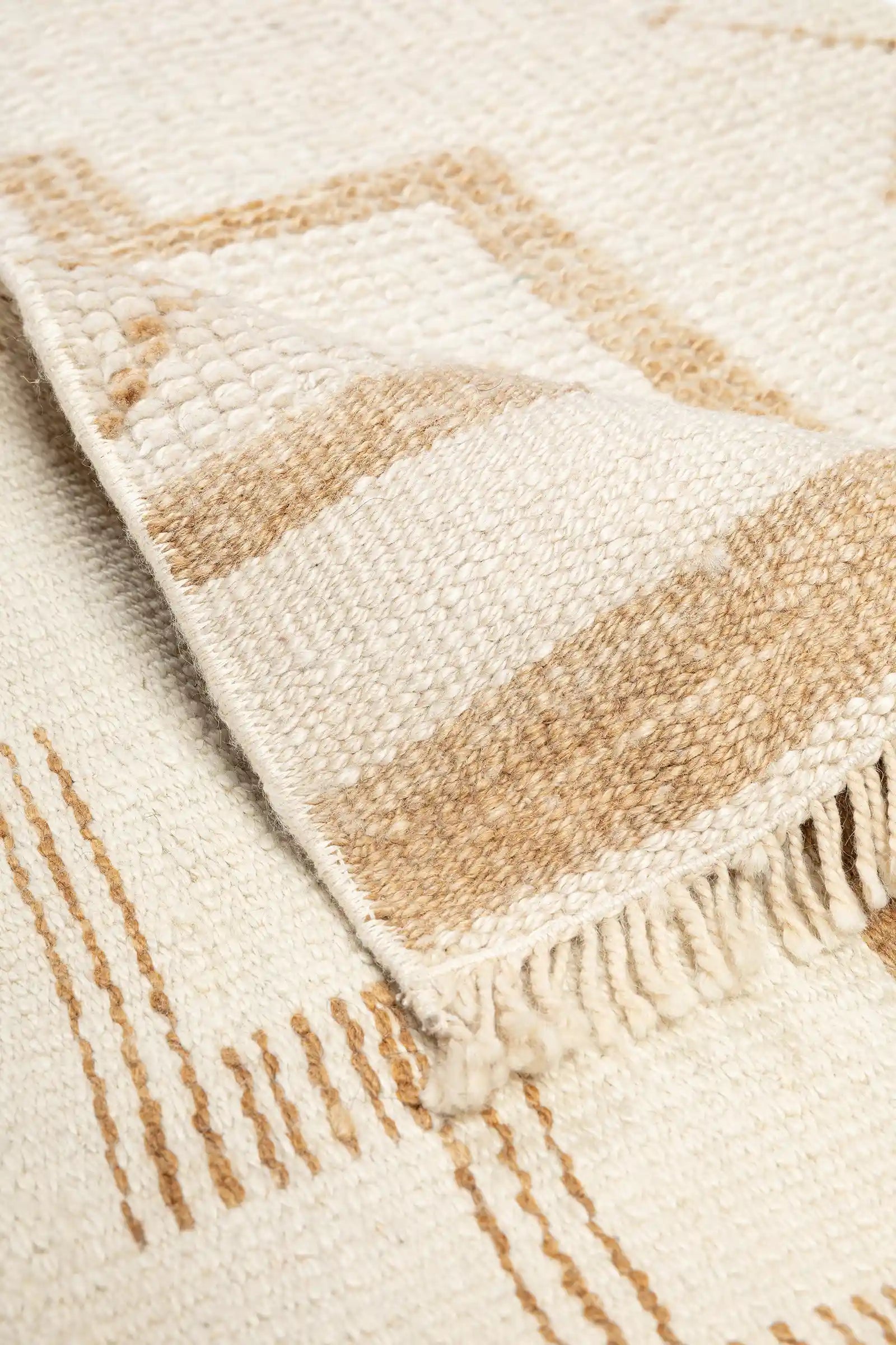 Detailansicht der Teppichkante mit sichtbarer Rückseite in gestreifter, beiger Webung und kurzen, geknoteten Fransen an der Kante.