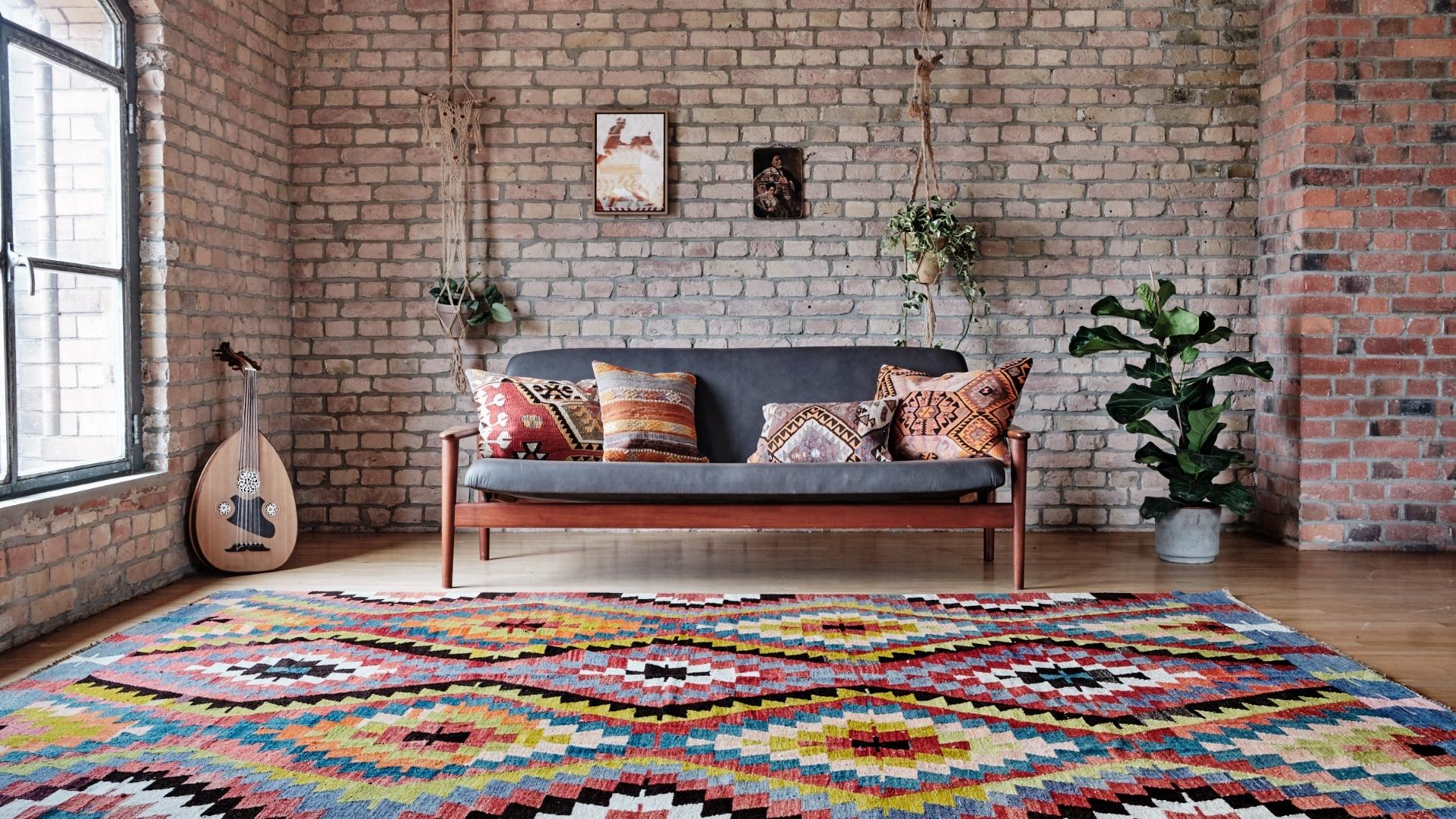 Großer Raum, der mit einem Holzsofa, auf dem Vintage Kelim Kissen liegen, und einem großen bunt gemusterten Kelim eingerichtet ist