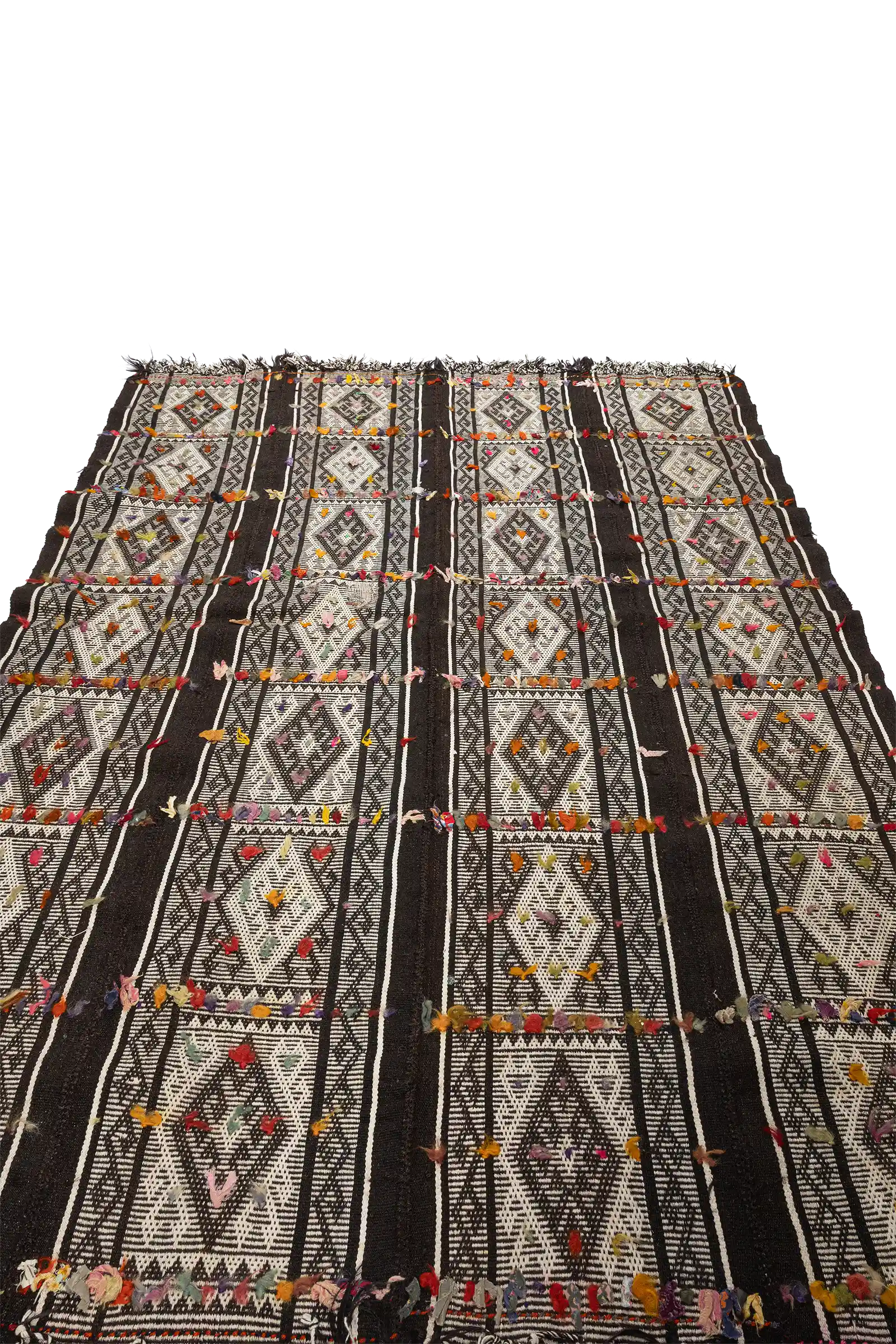 Diagonal aufgenommene Ansicht des Kilims mit symmetrischer Anordnung von weißen Rauten auf schwarzem Grund und verstreut platzierten bunten Garnakzenten entlang der Linien.