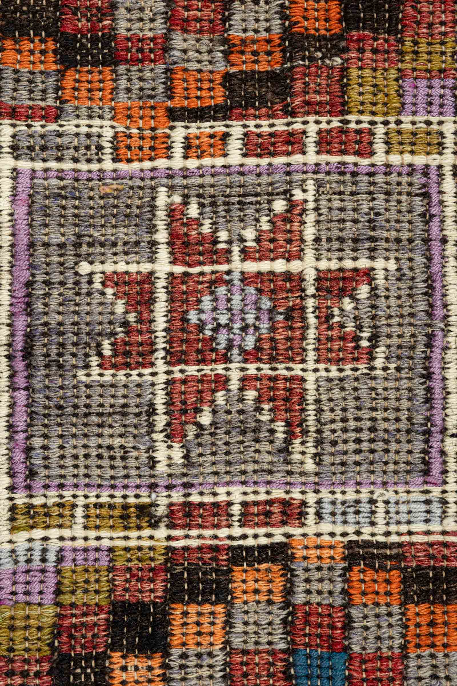Nahaufnahme eines rechteckigen Feldes mit einem sternförmigen Motiv in Lila und Creme auf olivgrünem Hintergrund. Umgeben von kleinteiligen Karomustern in Rot, Orange, Schwarz, Lila und Blau sowie geometrischem Umrandungsmuster in Weiß und Lila.