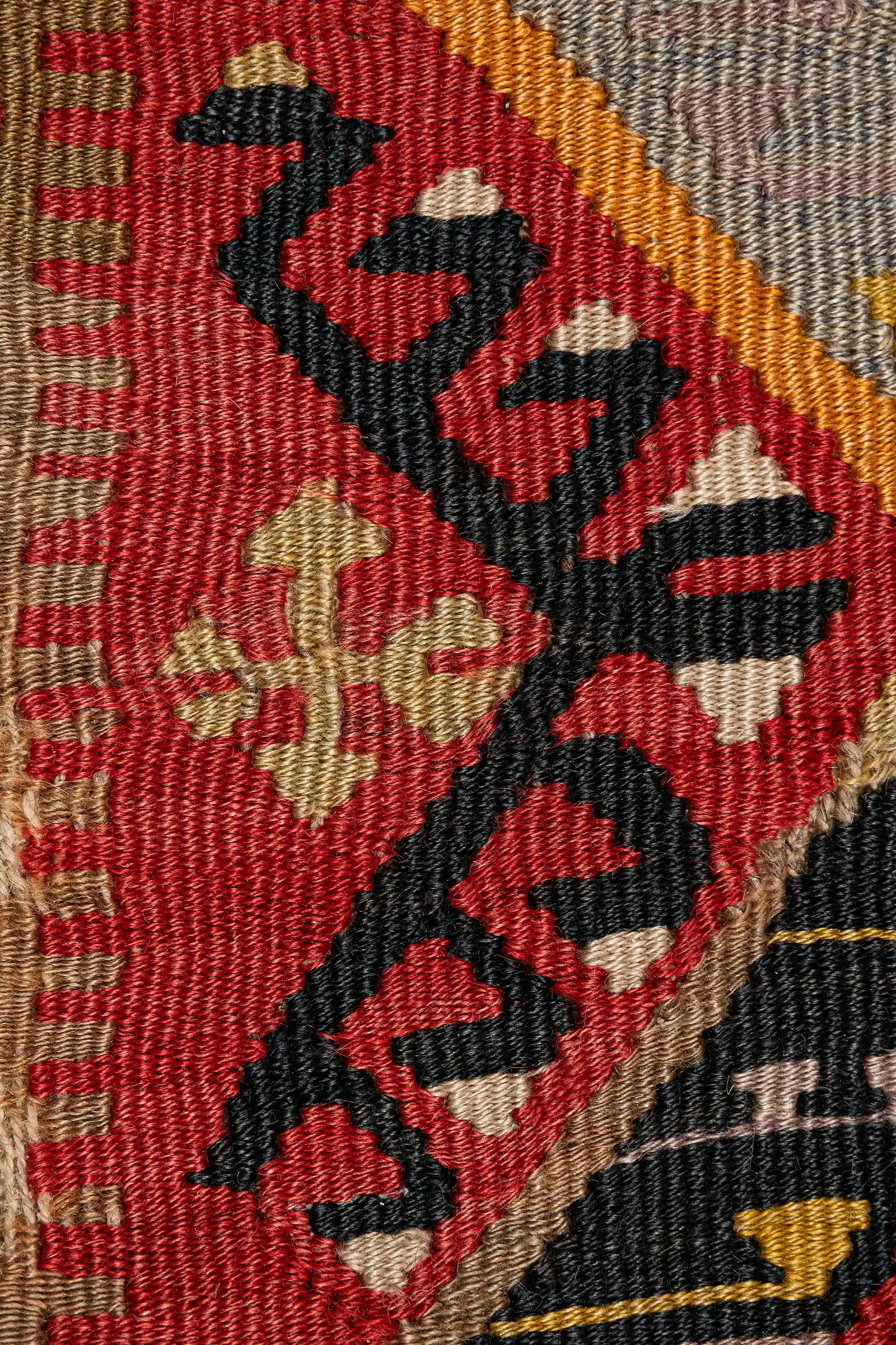 Nahaufnahme eines diagonalen schwarzen Zickzack-Motivs auf rotem Grund, eingefasst von feinen Linien in Beige und Orange. Die Webstruktur ist eng und glatt, mit leicht glänzender Oberfläche.