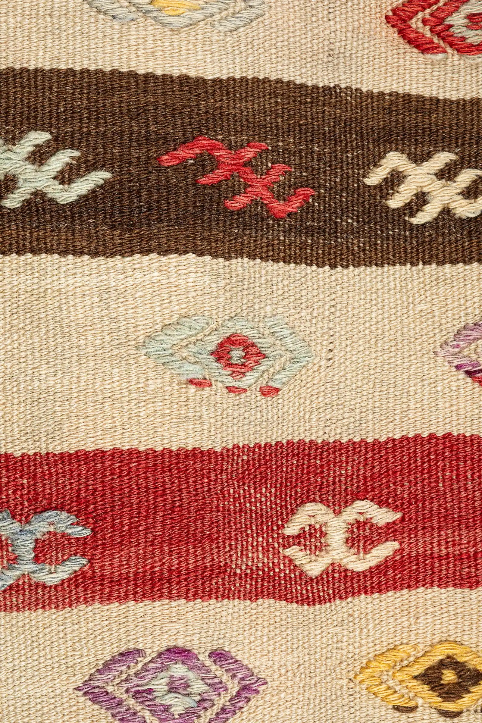 Detailaufnahme der Streifen – hellbraune, rötliche und beigefarbene Streifen mit eingewebten Mustern in Hellblau, Rot, Violett und Beige, darunter kleine Hakenformen, Rauten und gestickte Motive