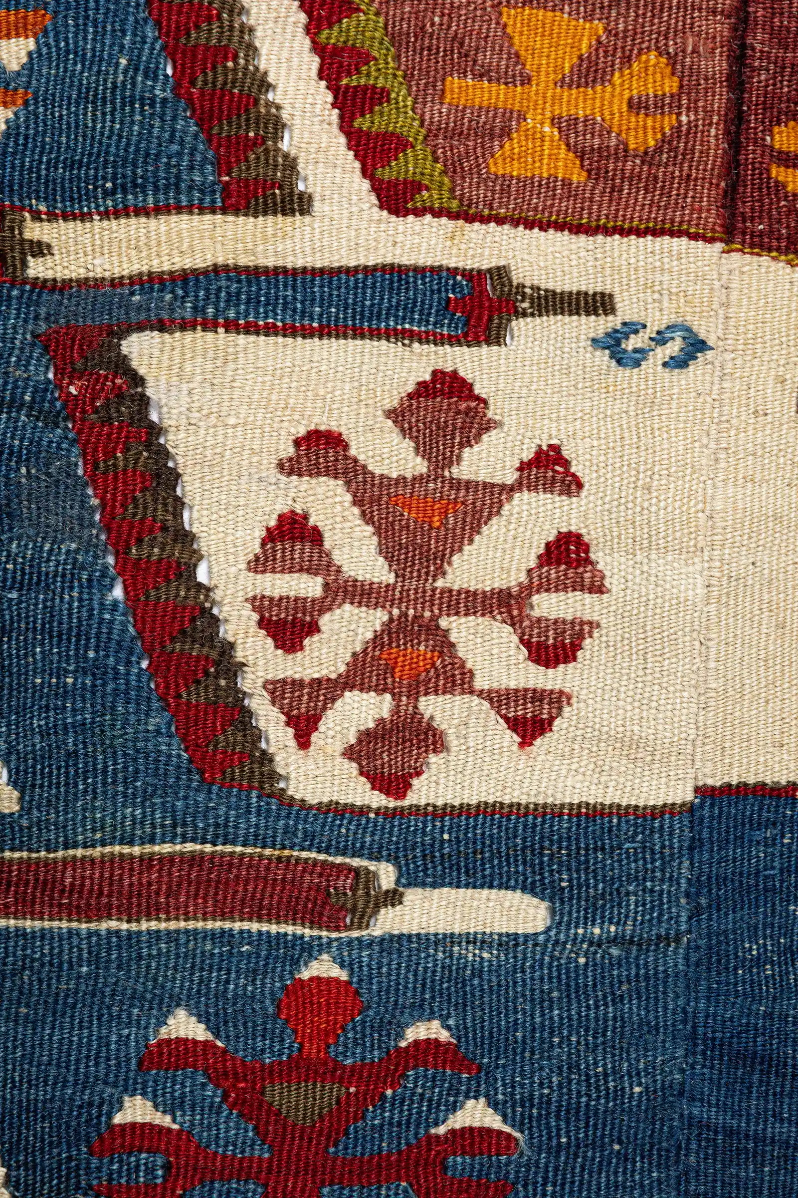 Nahansicht eines mittigen Kelimbereichs mit roten, weißen und braunen Musterelementen auf naturfarbenem Grund, detaillierte Webstruktur erkennbar.

