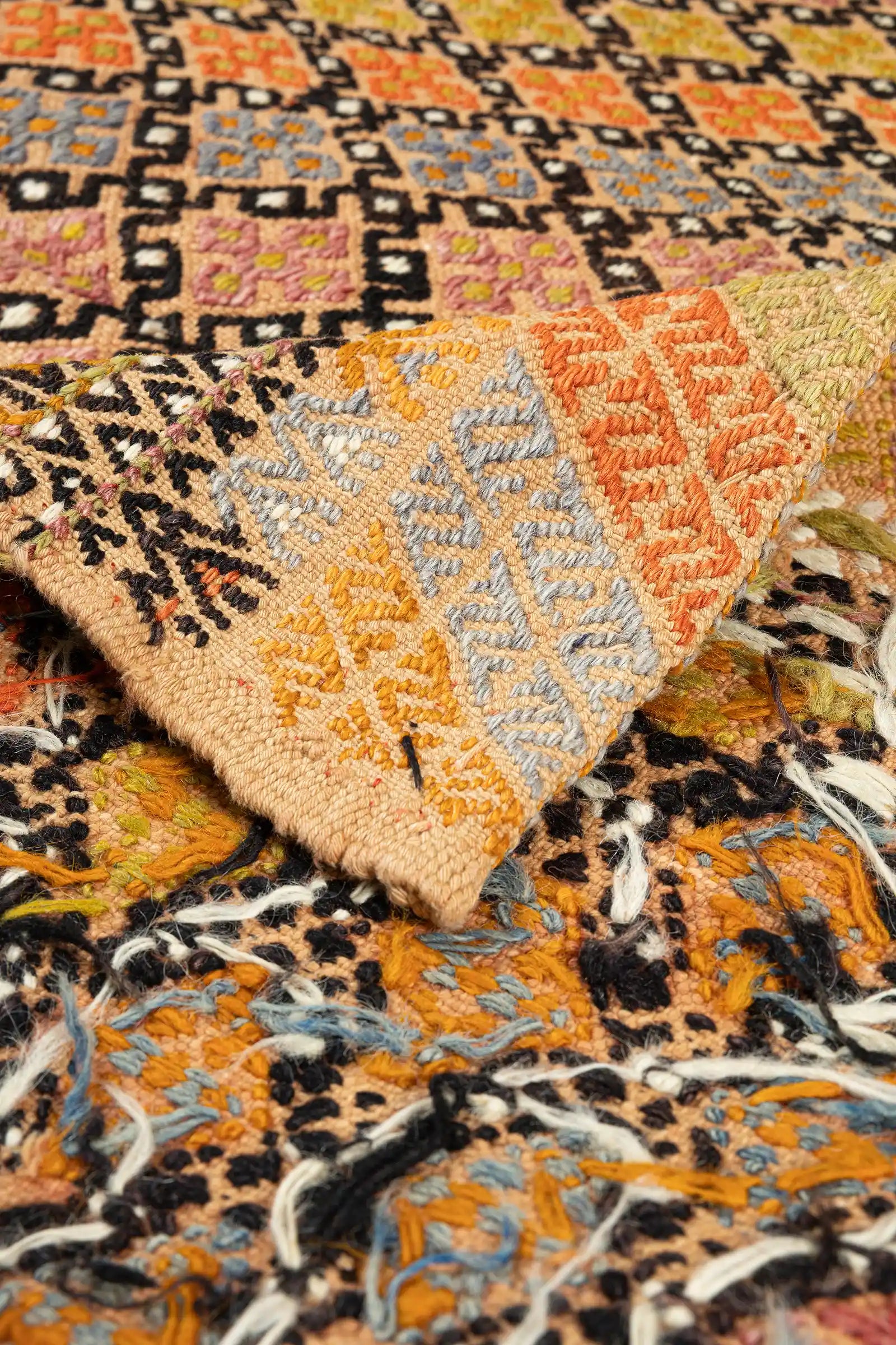 Vorder- und Rückseite des Kilims übereinandergelegt: oben die feine Knotenstruktur mit kräftigen Farbfeldern in Orange, Hellblau und Gelb; darunter die offenliegende Rückseite mit lockerem Garn, hellen Fransen und sichtbarem Webmuster.