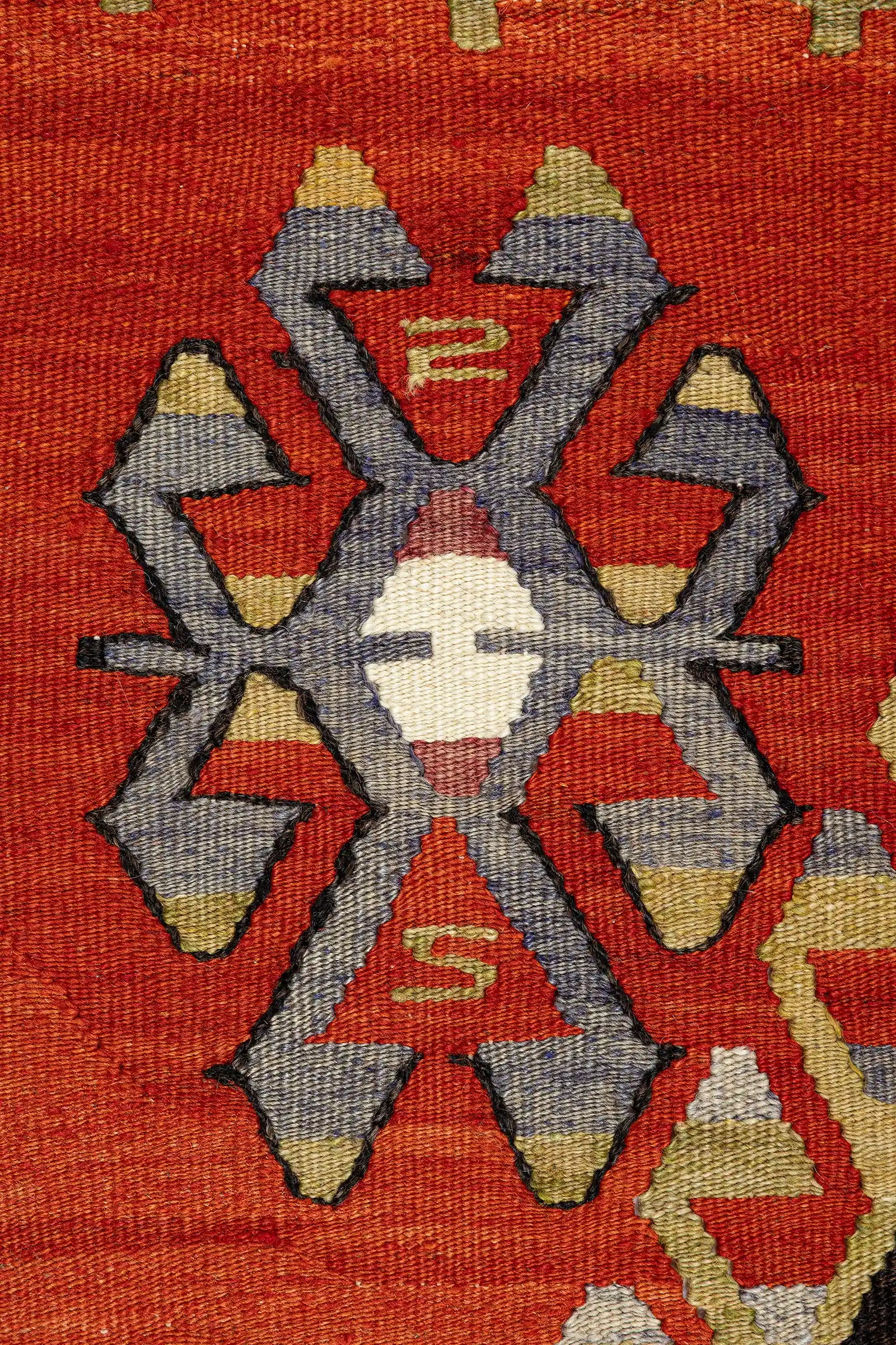 Detailaufnahme eines geometrischen Motivs – kantige, verschachtelte Form in Violett, Beige und Graublau auf kräftig rotem Hintergrund