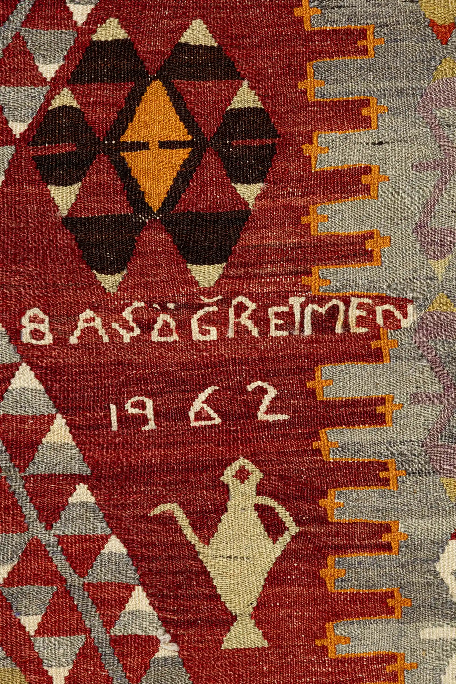 Nahaufnahme eines der zentralen Medaillons mit gezacktem Innenmuster in Schwarz, Gelb, Grau und Weiß, eingefasst von roten Rauten. Umgeben von weißen Flächen mit kleinen, farblich abgesetzten Kreuzmotiven.