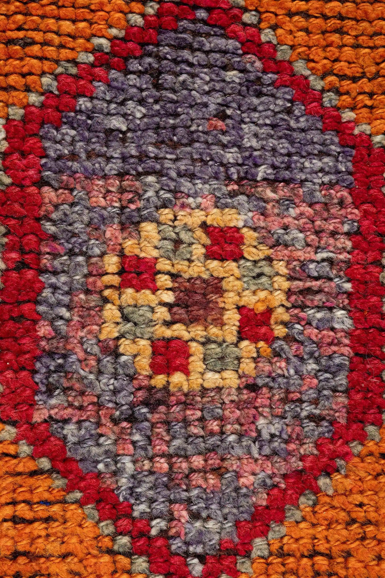 Zentrale Aufnahme eines orangefarbenen Medaillons mit violettem Zentrum und roten Konturen, eingerahmt von gezackten Linien und flankiert von traditionellen Ornamenten auf intensiv rostrotem Grund.